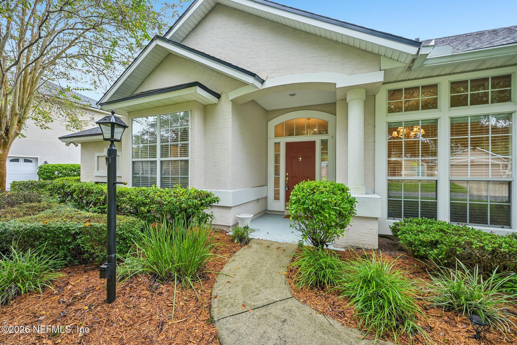 Home exterior with a red front door, covered entry, landscaped beds, and a curved walkway.