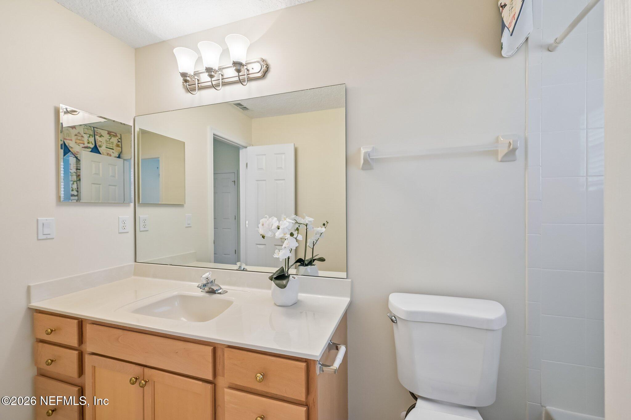 Bathroom with a wood vanity, large mirror, white toilet, and orchid on the counter.