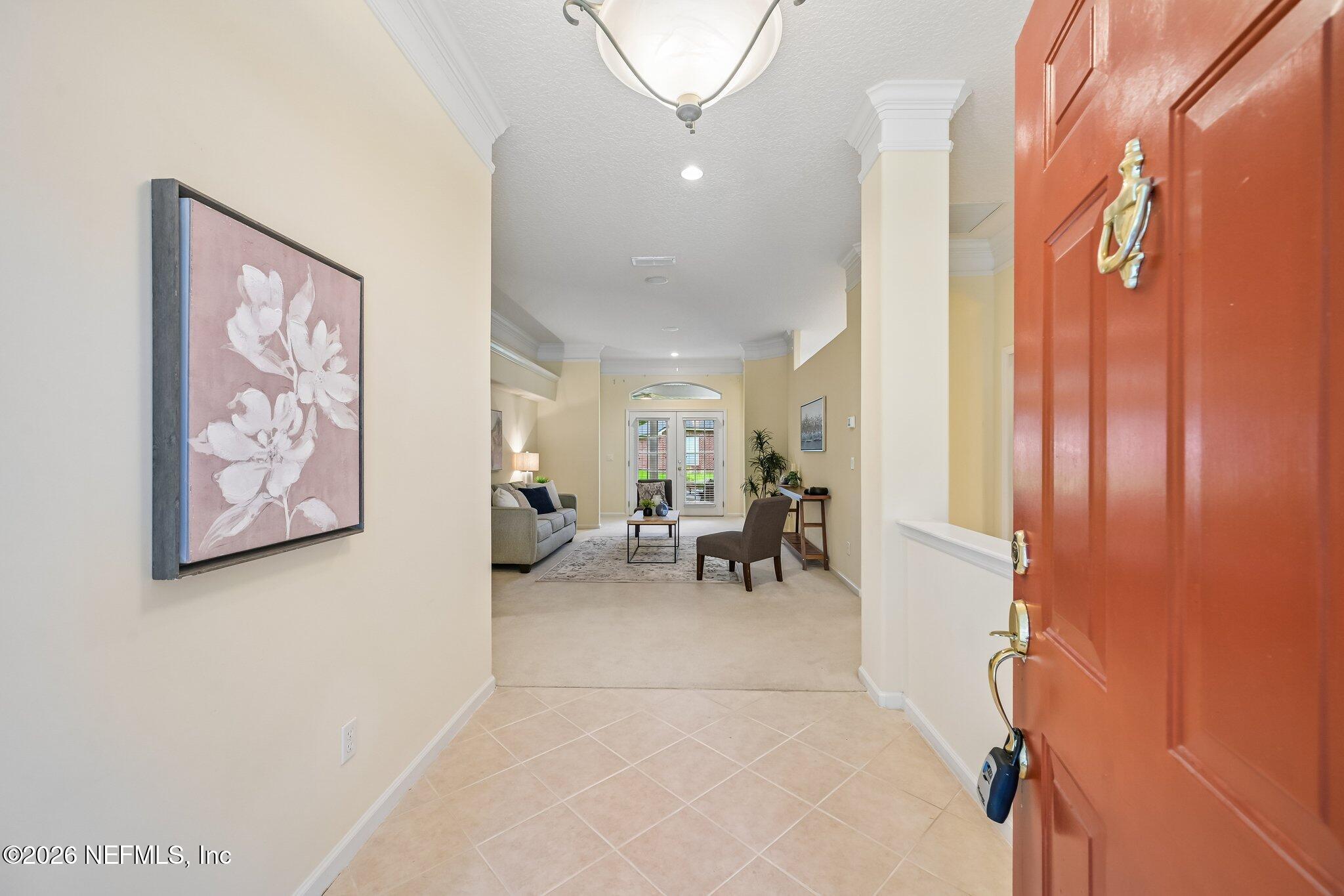 Tiled entry foyer with an open red front door and furnished living room beyond.