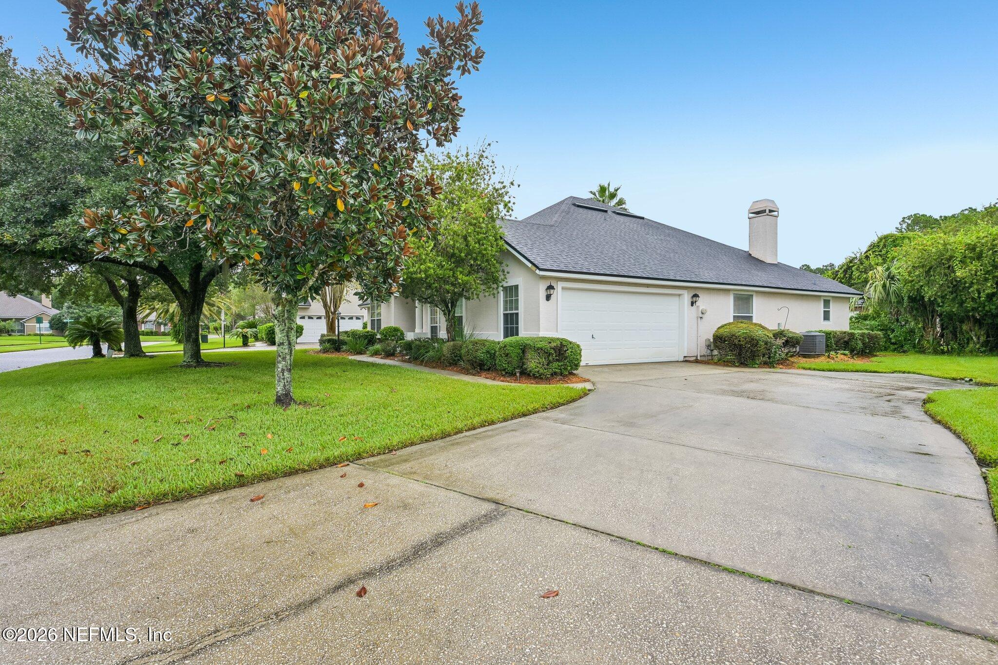 Single-story home with an attached garage, curved driveway, mature trees, and landscaped lawn.