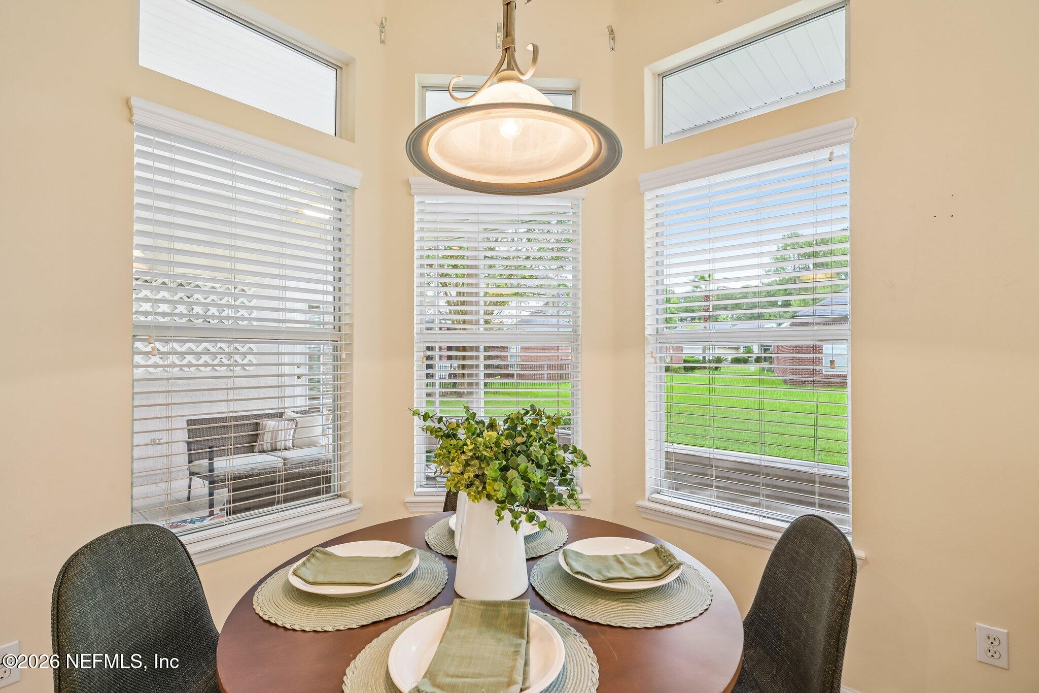 Dining nook with a set round table, leafy centerpiece, and three windows overlooking a lawn.