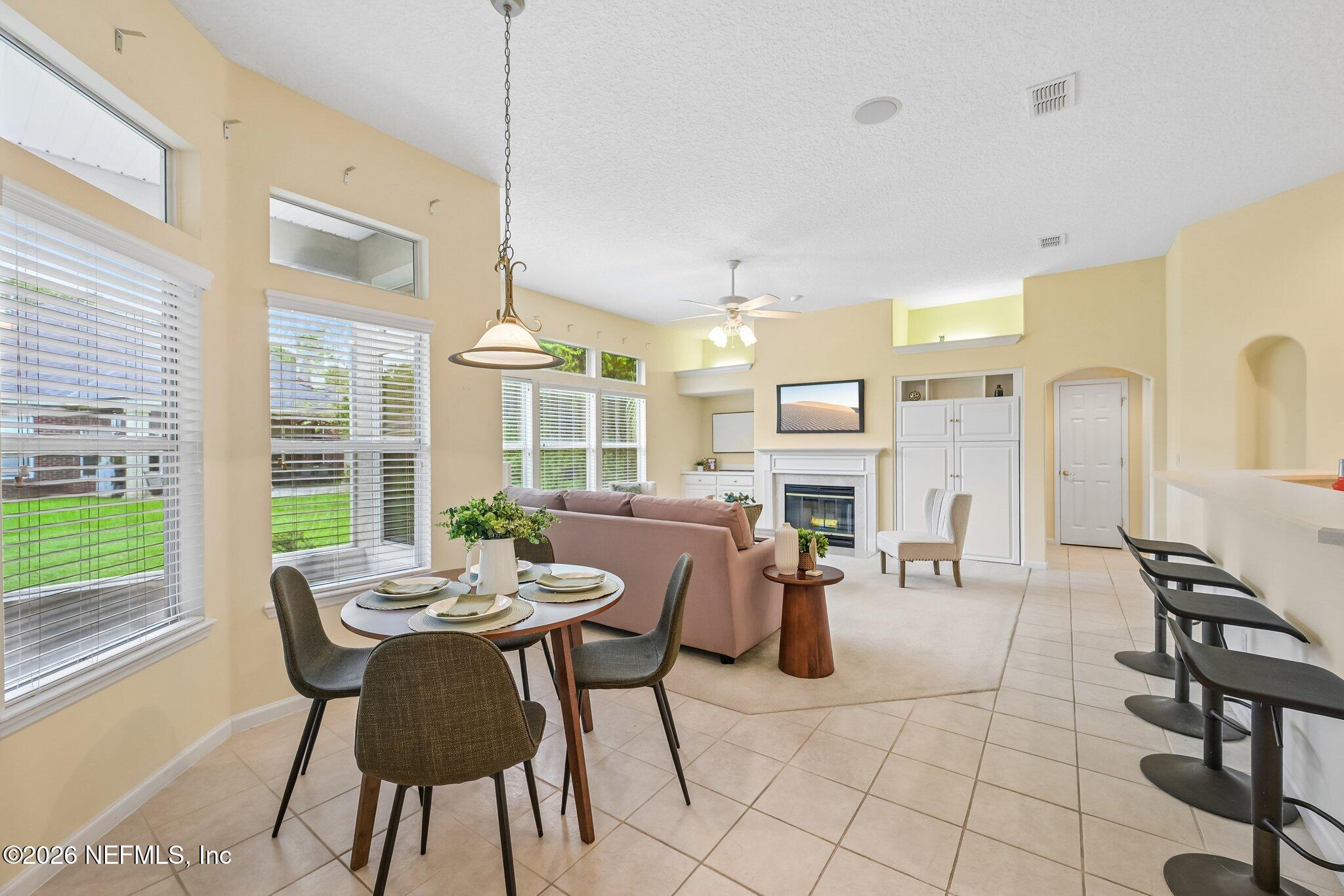 Open-plan living and dining room with large windows, a fireplace, and a kitchen island with bar stools.