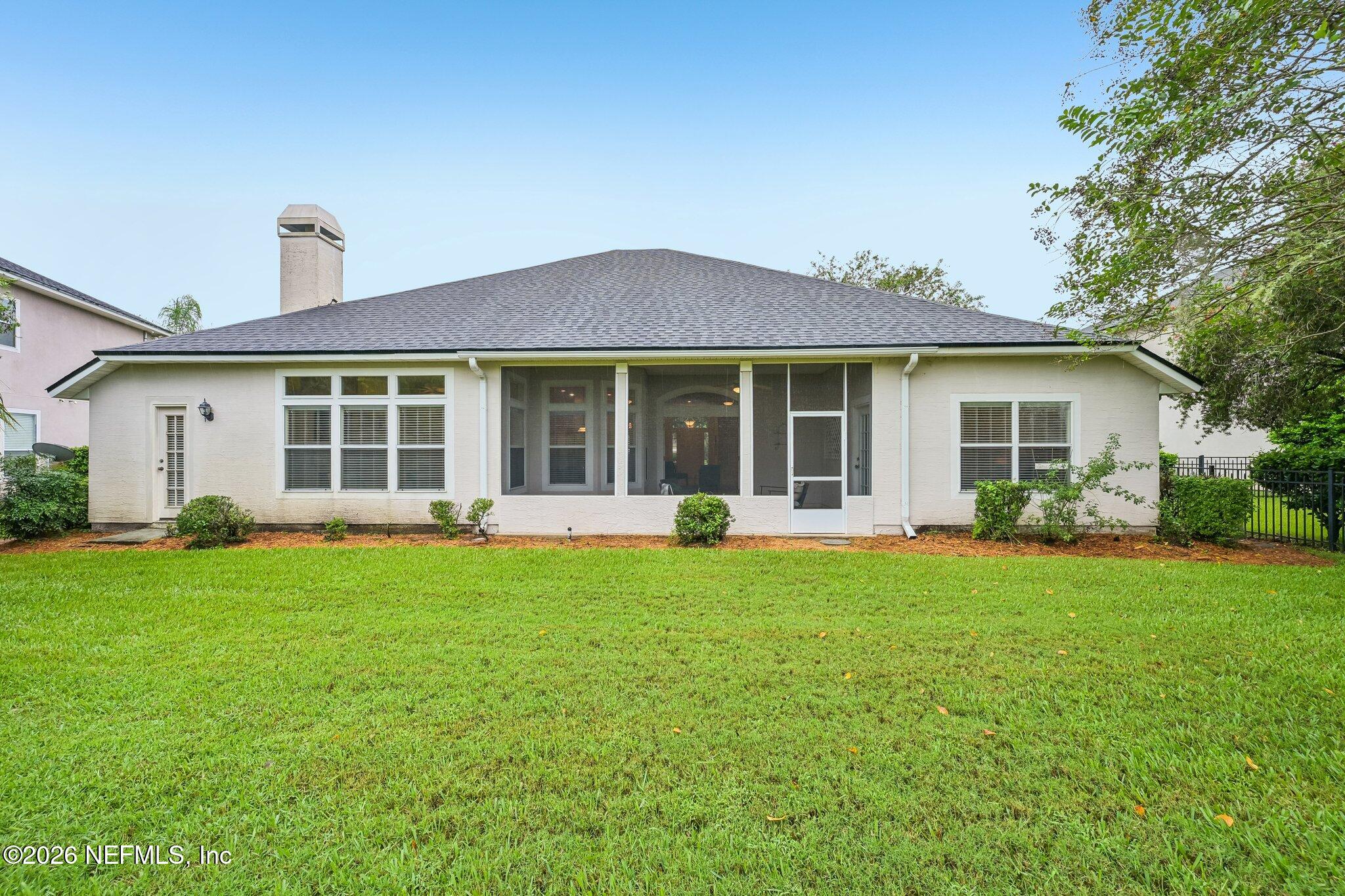 Rear of a white house with a screened porch and broad green lawn.