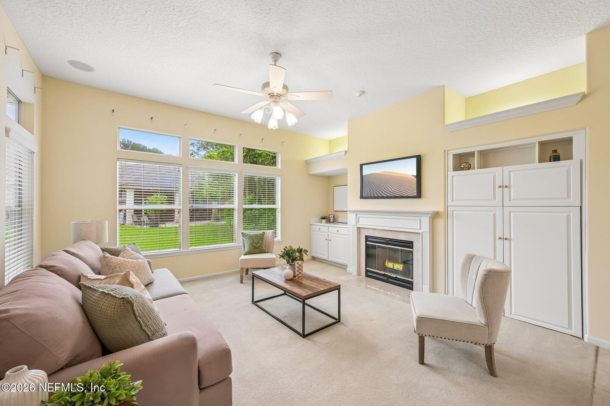 Living room with a fireplace, white built-ins, tall windows, and neutral furnishings.