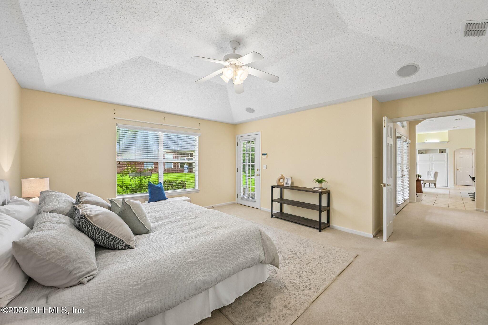 Staged bedroom with a large white-and-gray bed, vaulted ceiling, and glass-paneled door.