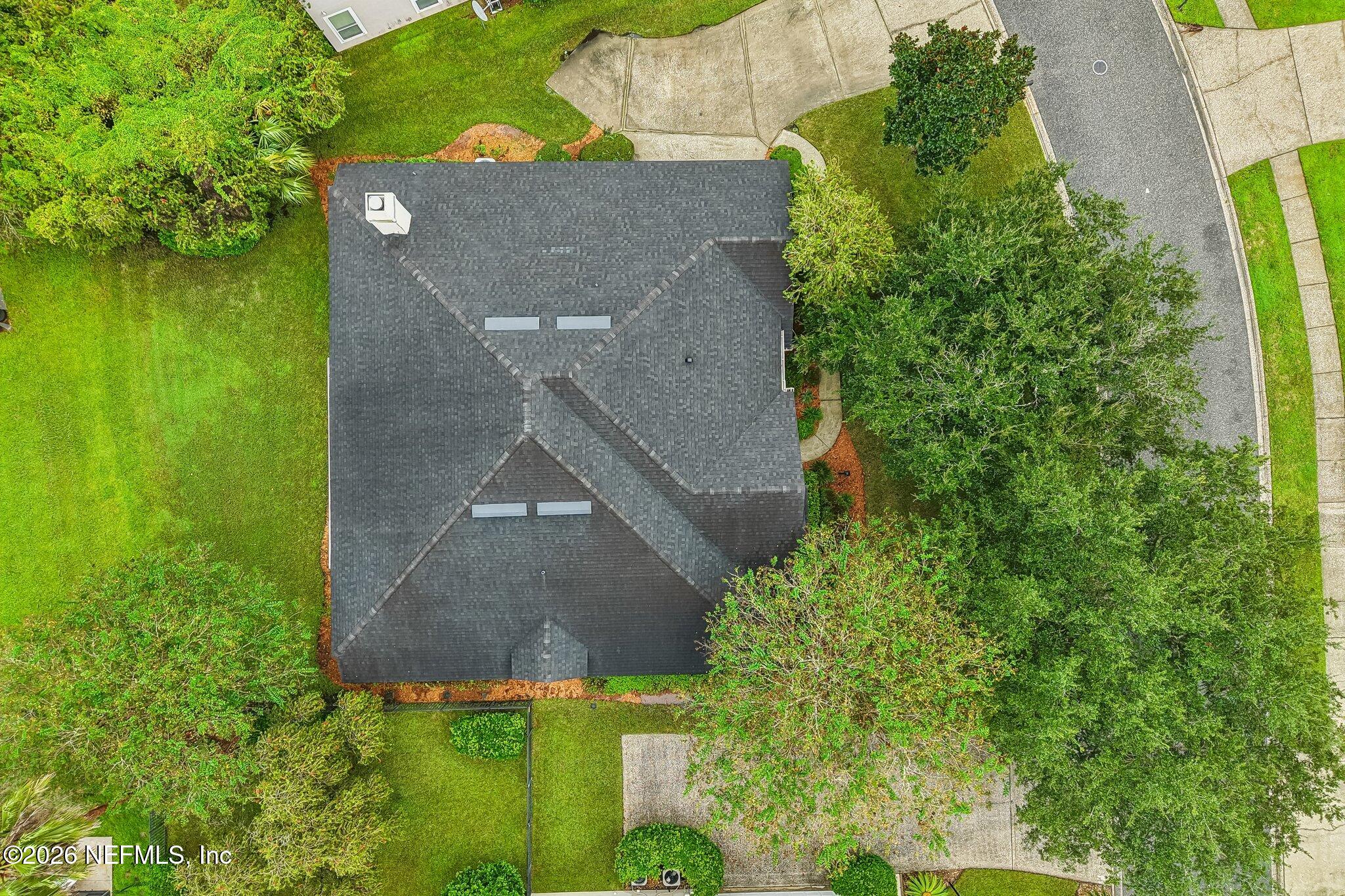 Aerial view of a house with a dark shingle roof amid a green lawn and mature trees.