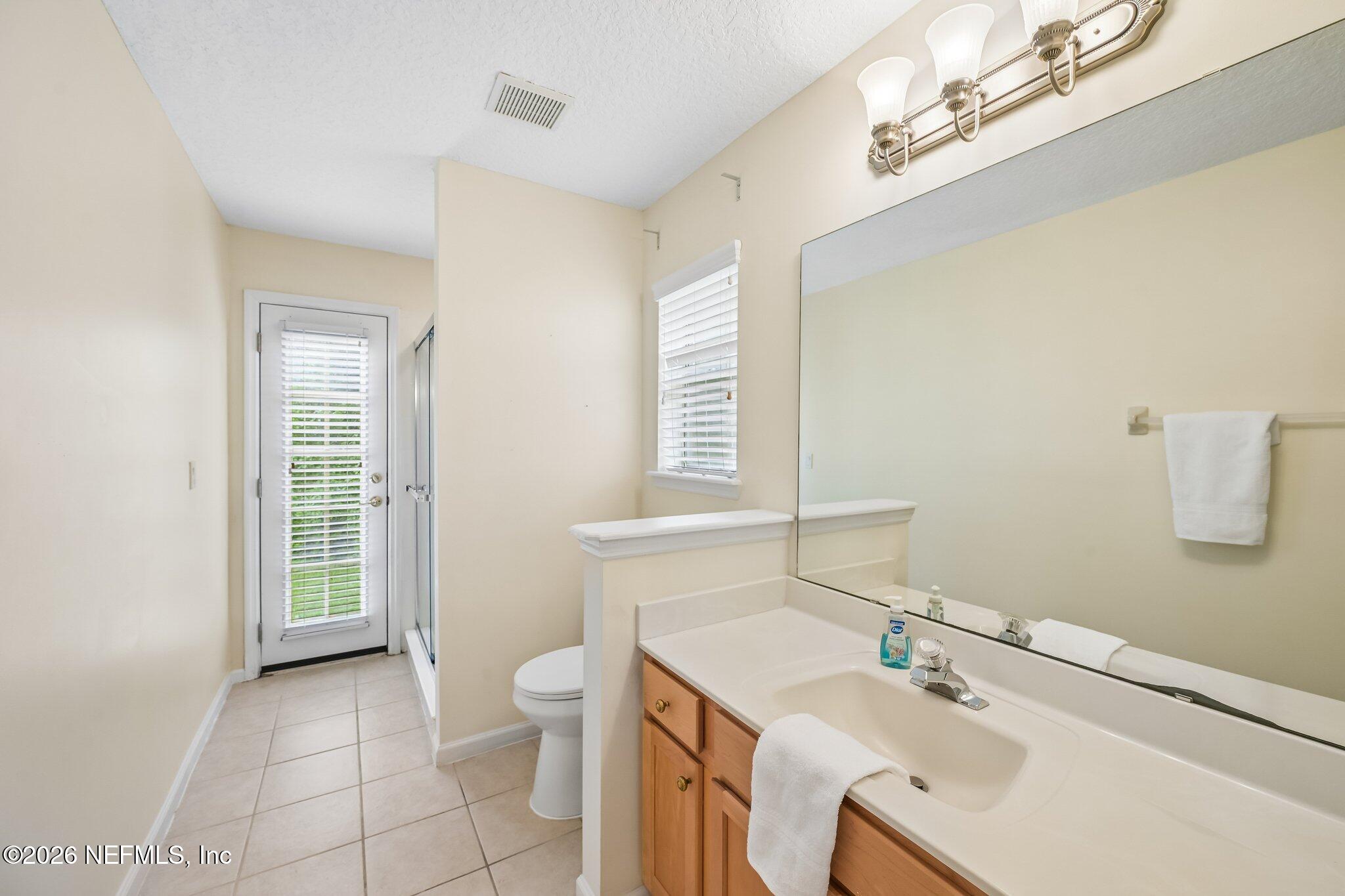 Bathroom with a wood vanity and large mirror, tiled floor, and a door with blinds.
