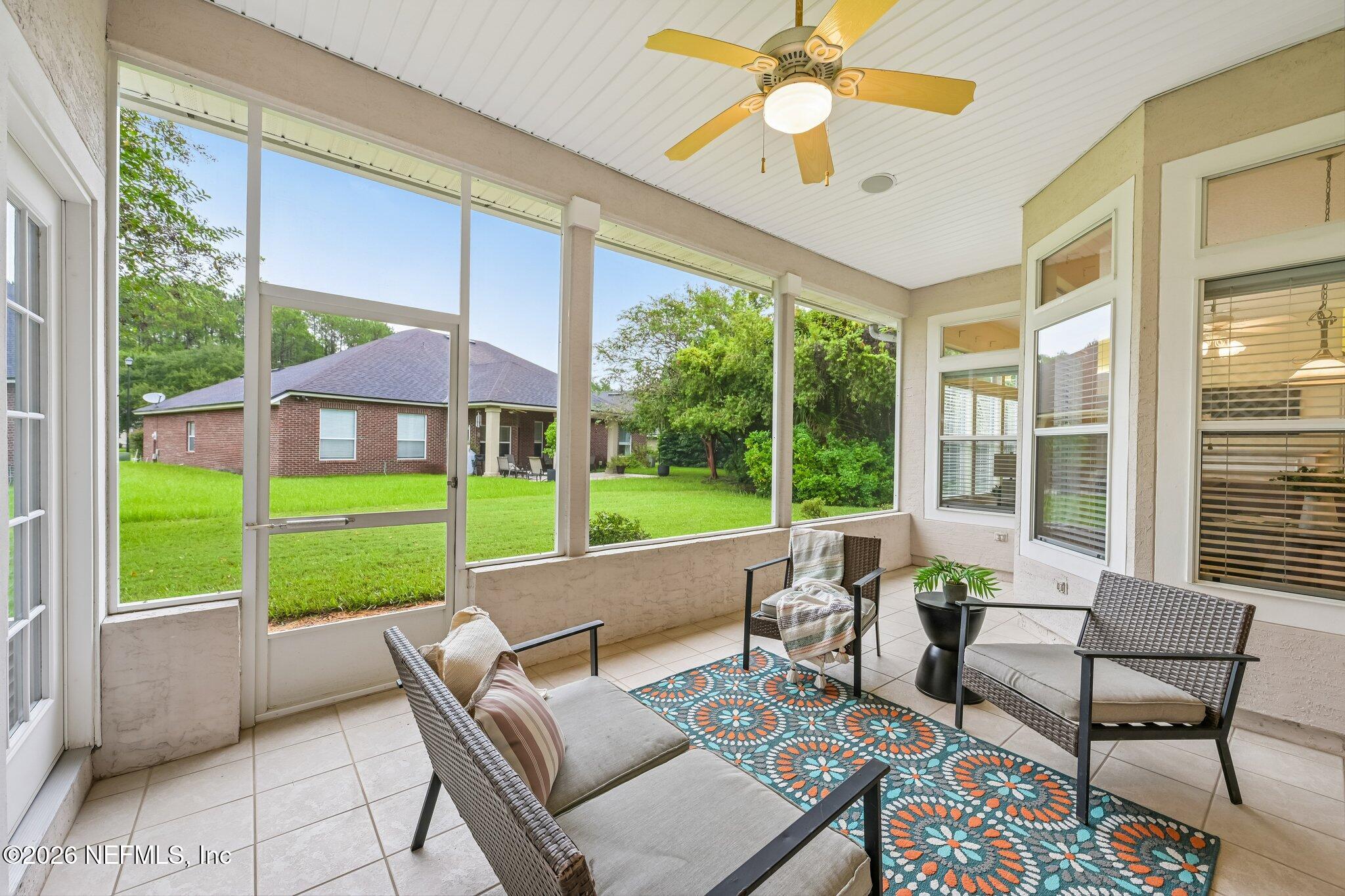 Screened porch with wicker seating, a colorful rug, and views of the lawn and trees.