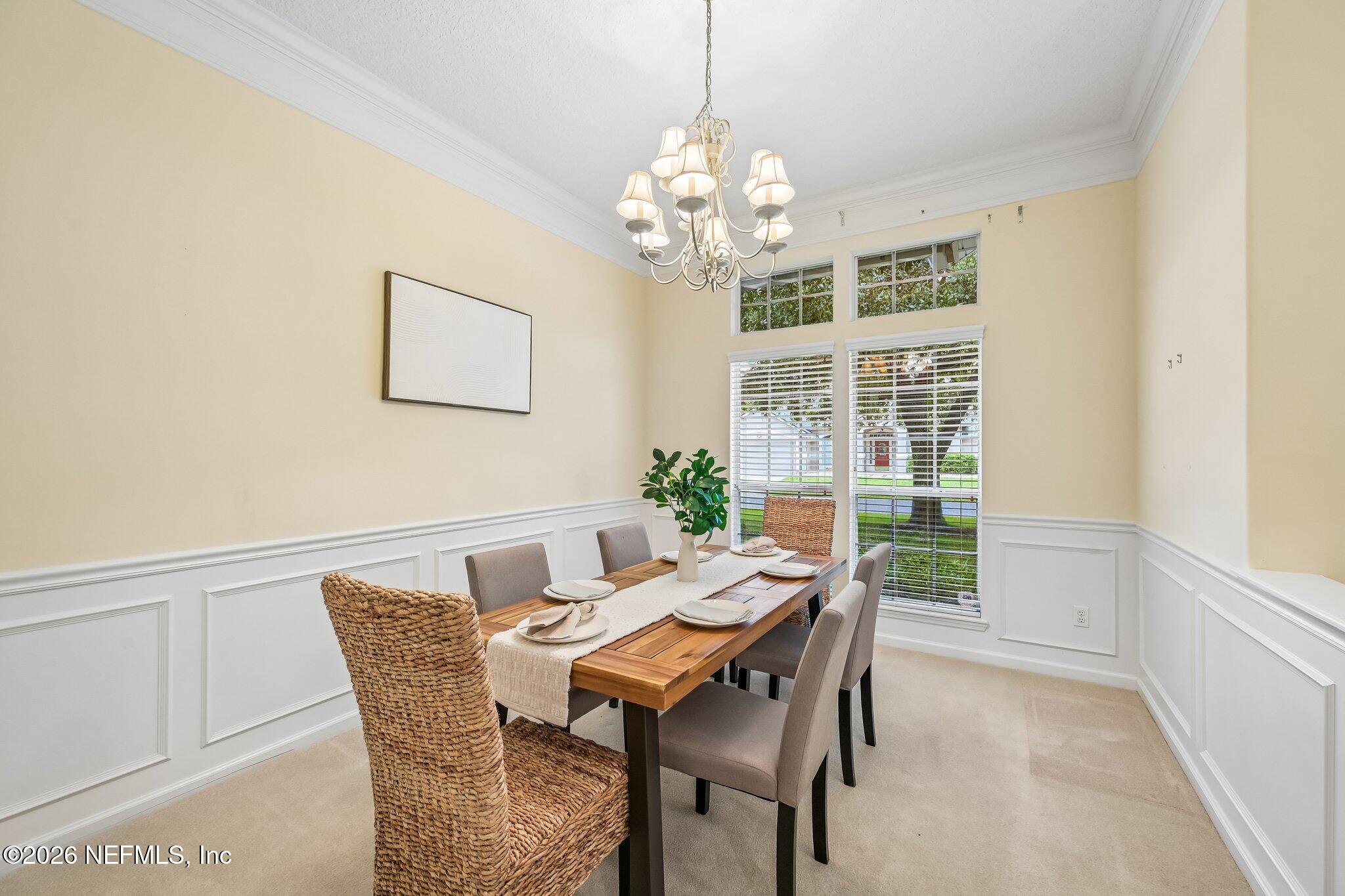 Staged dining room with a wooden table, chandelier, and tall windows overlooking the lawn.