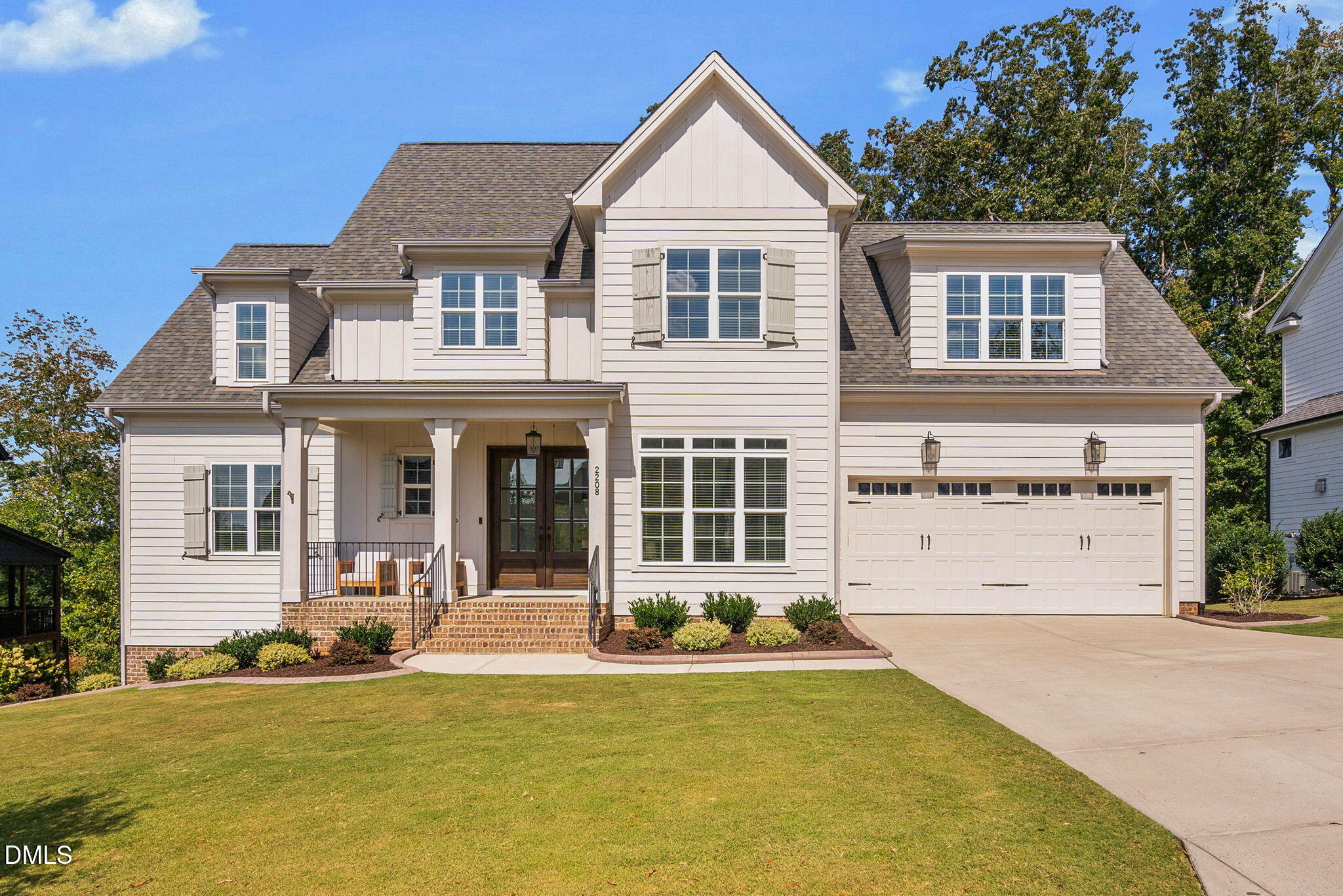 Two-story white house with a covered brick porch, landscaped lawn, and attached two-car garage.