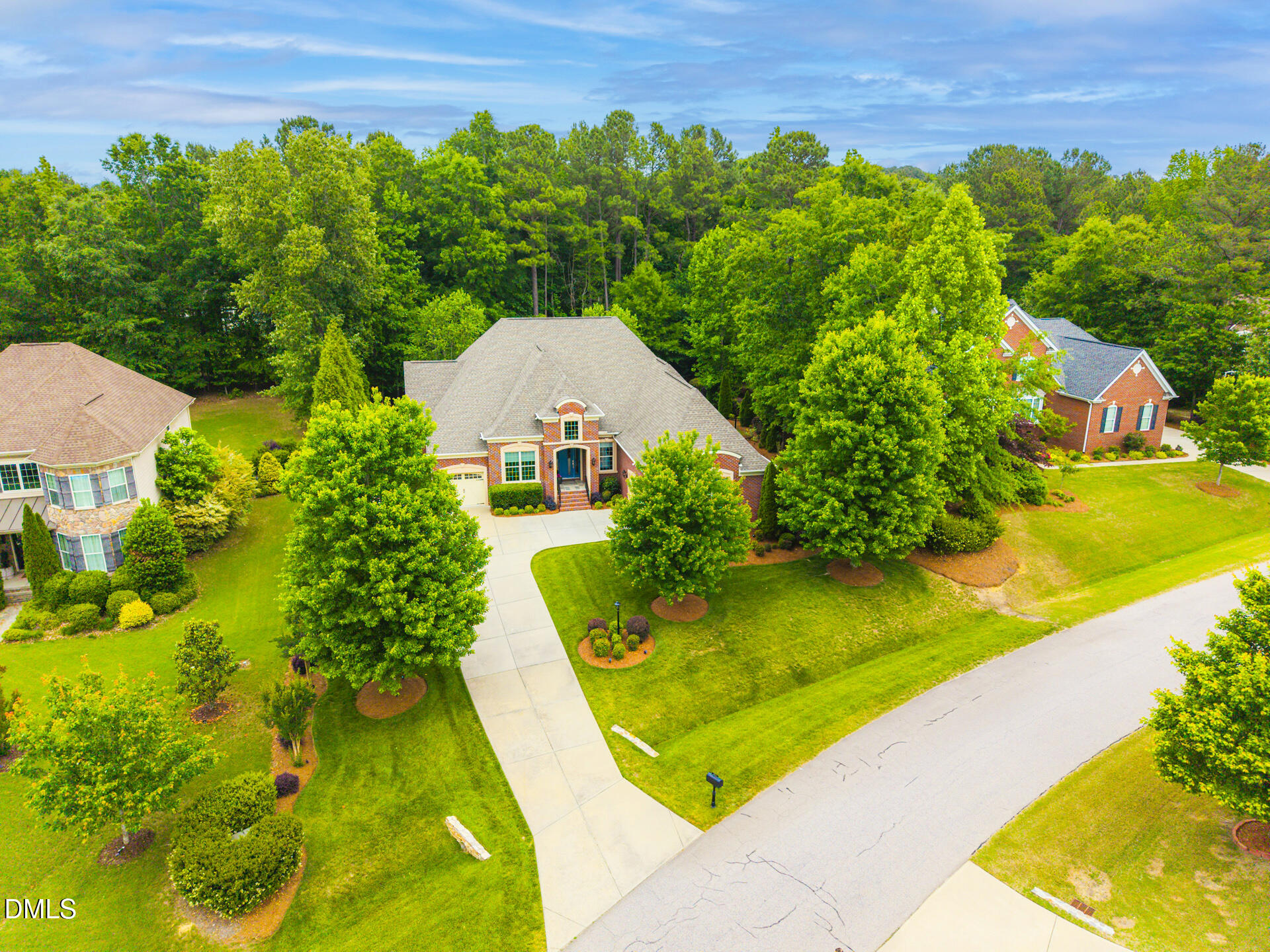 Aerial view of a brick house with a curved driveway, landscaped lawn, and mature trees.
