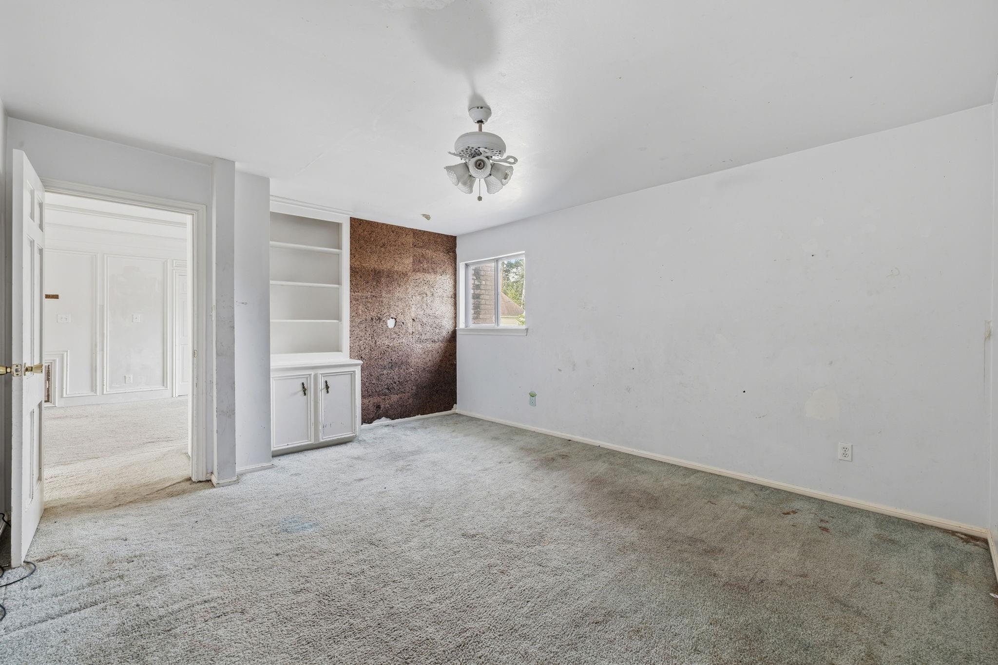 Empty carpeted room with built-in shelving, a small window, and a ceiling fan.