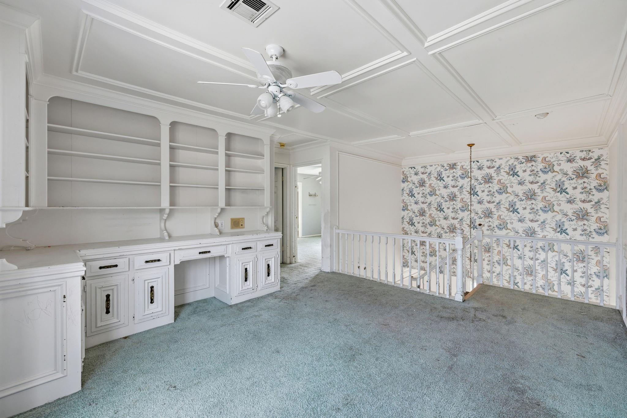Carpeted landing with built-in white shelving, a ceiling fan, floral wallpaper, and stair railing.