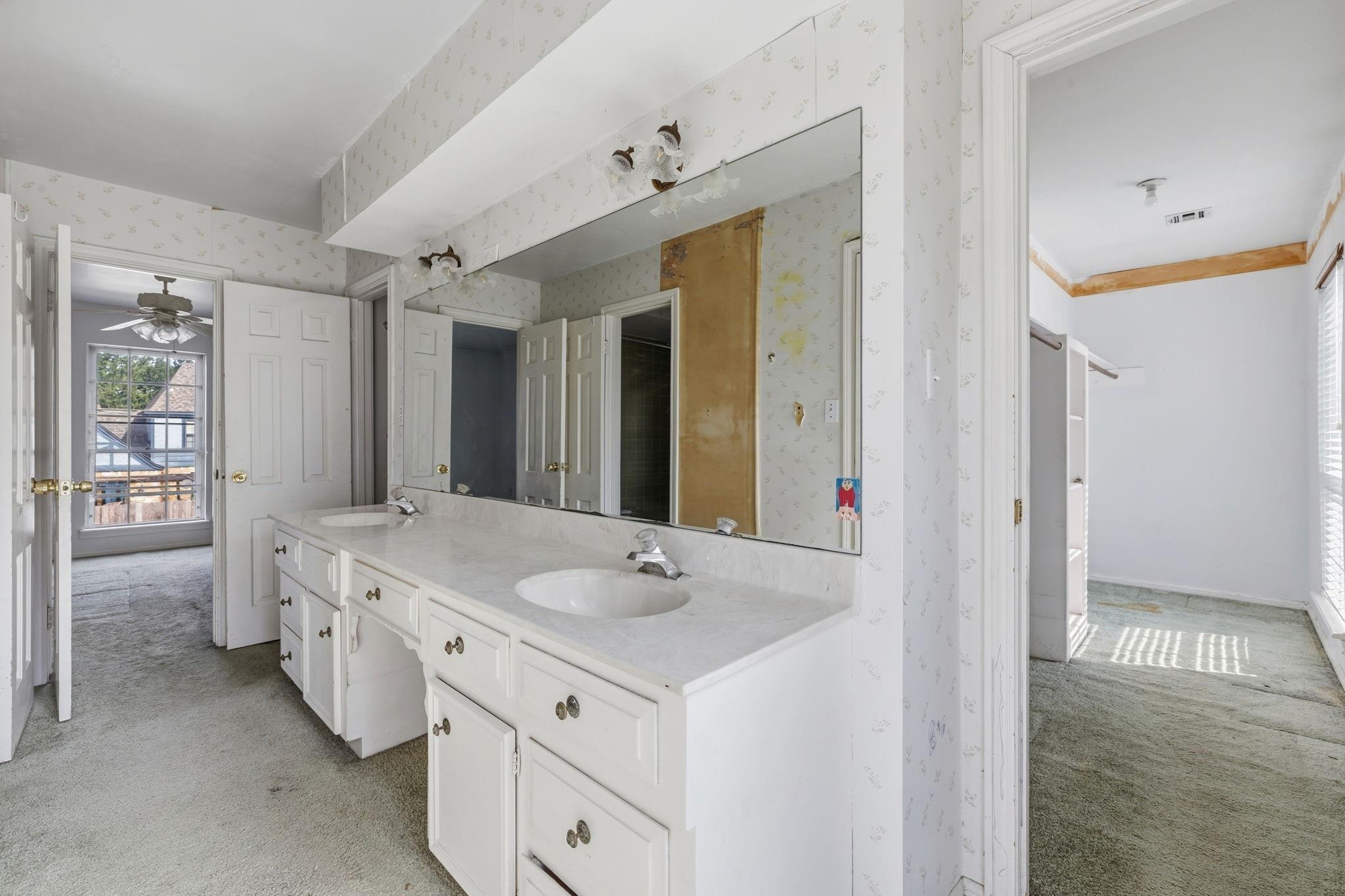 Bathroom with a long white double-sink vanity and a large mirror beside open doorways.