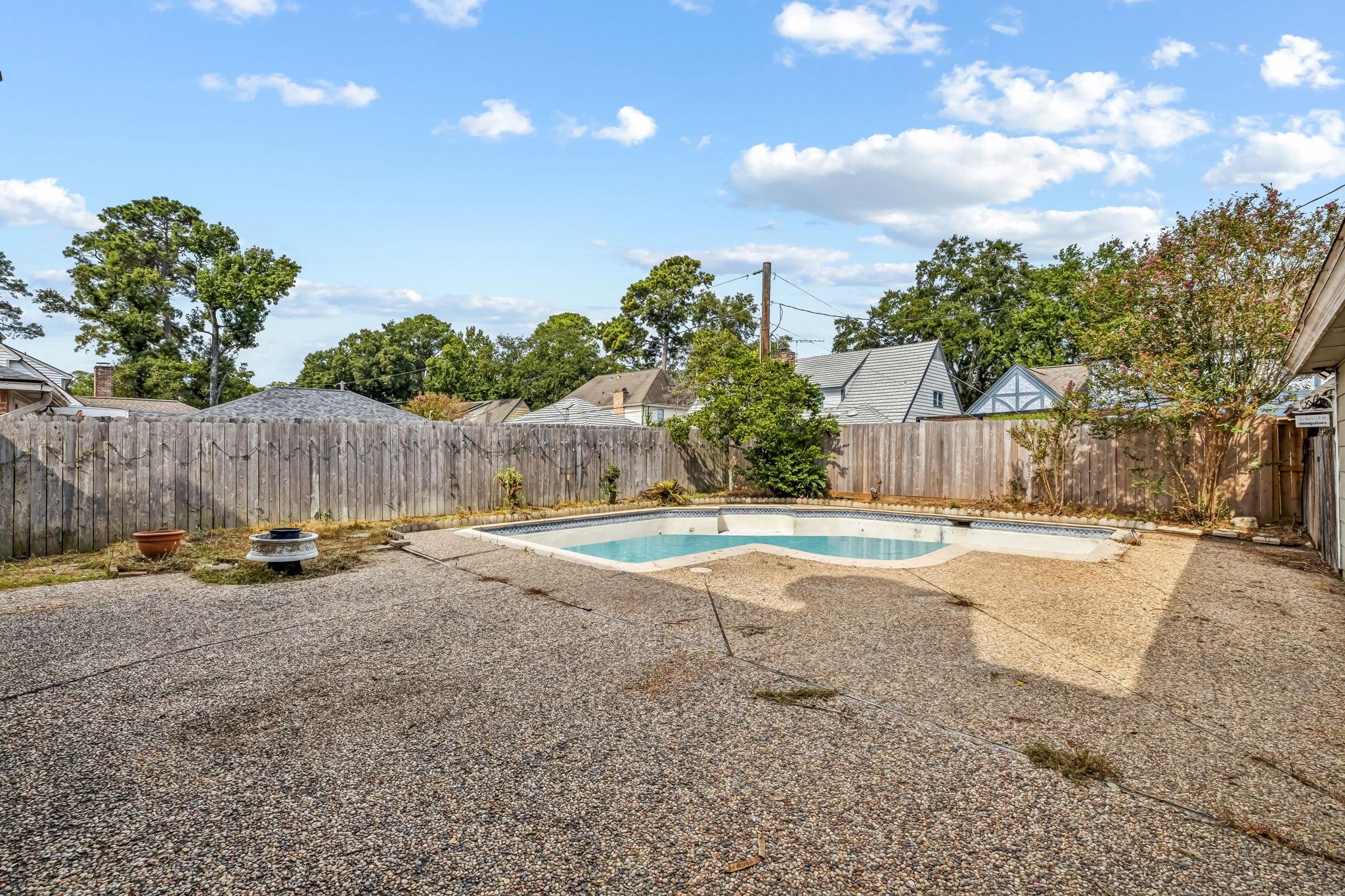 Backyard pool and broad pebble-finish patio enclosed by a wooden fence.
