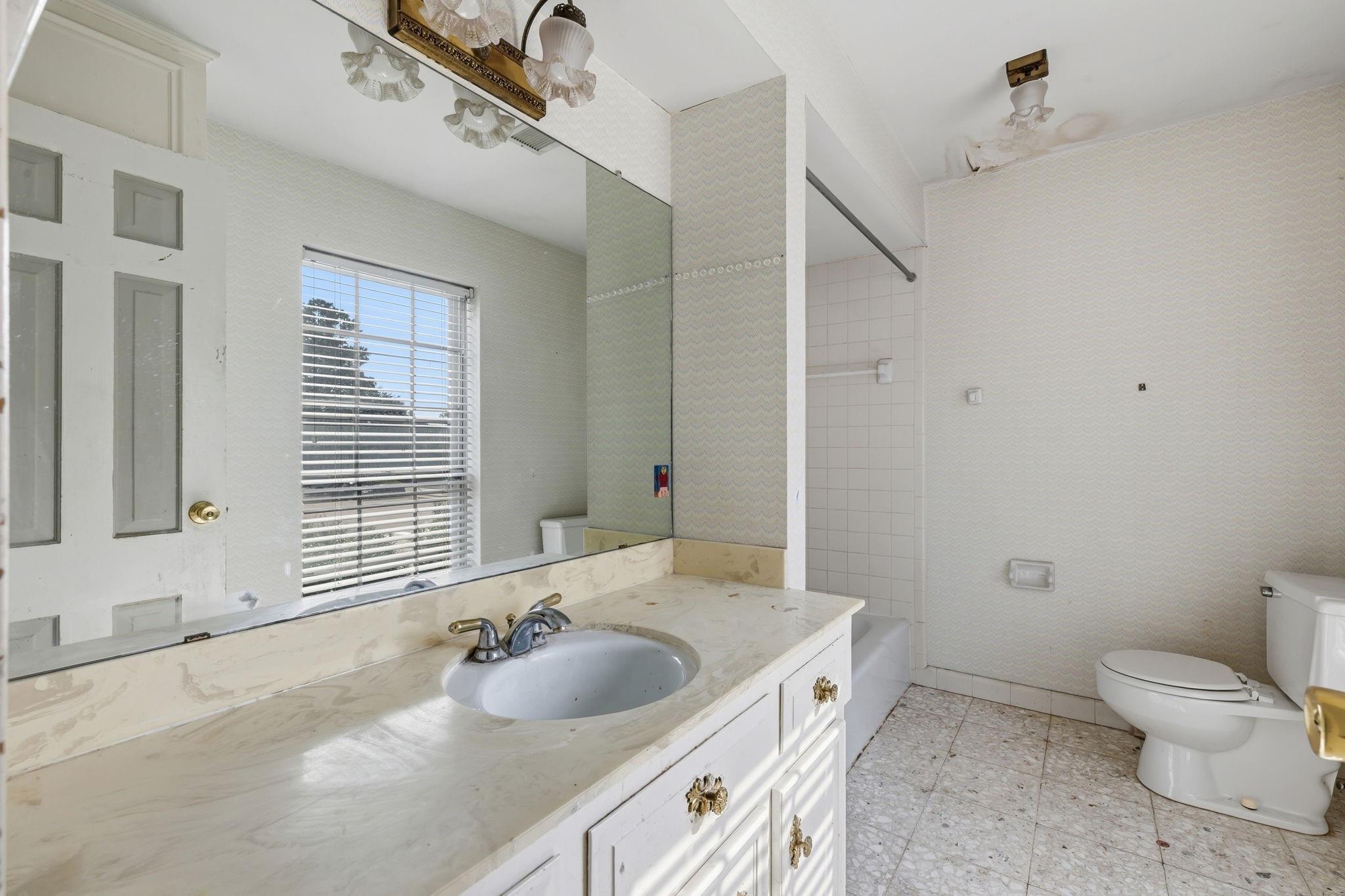Bathroom with a long vanity, large mirror, window blinds, bathtub, and toilet.