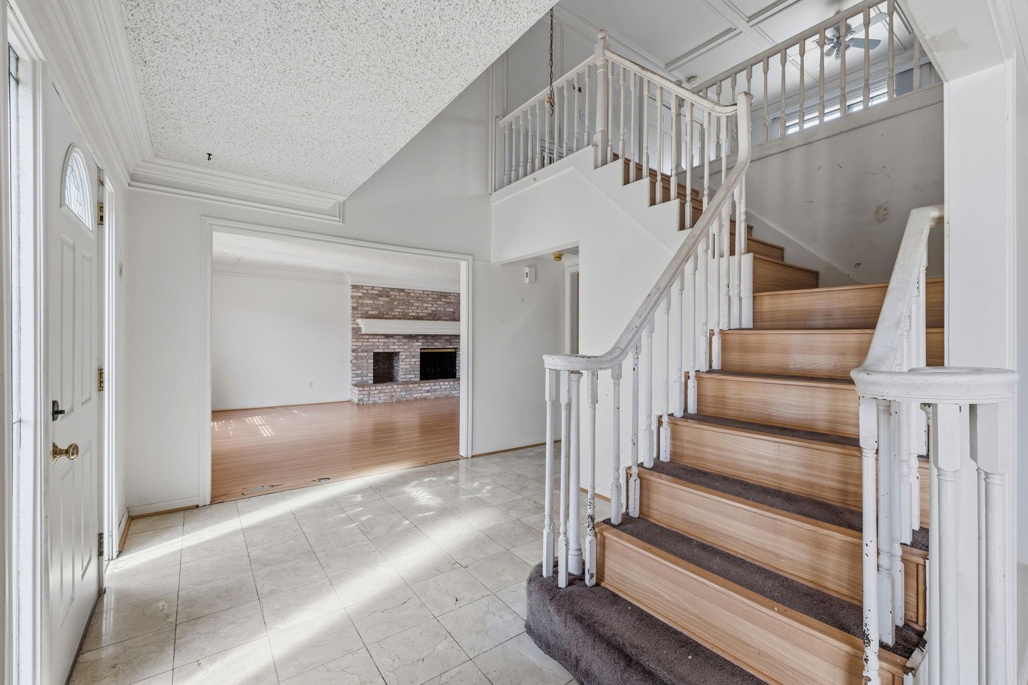 Two-story entry foyer with a wooden staircase and an adjoining living room with a brick fireplace.