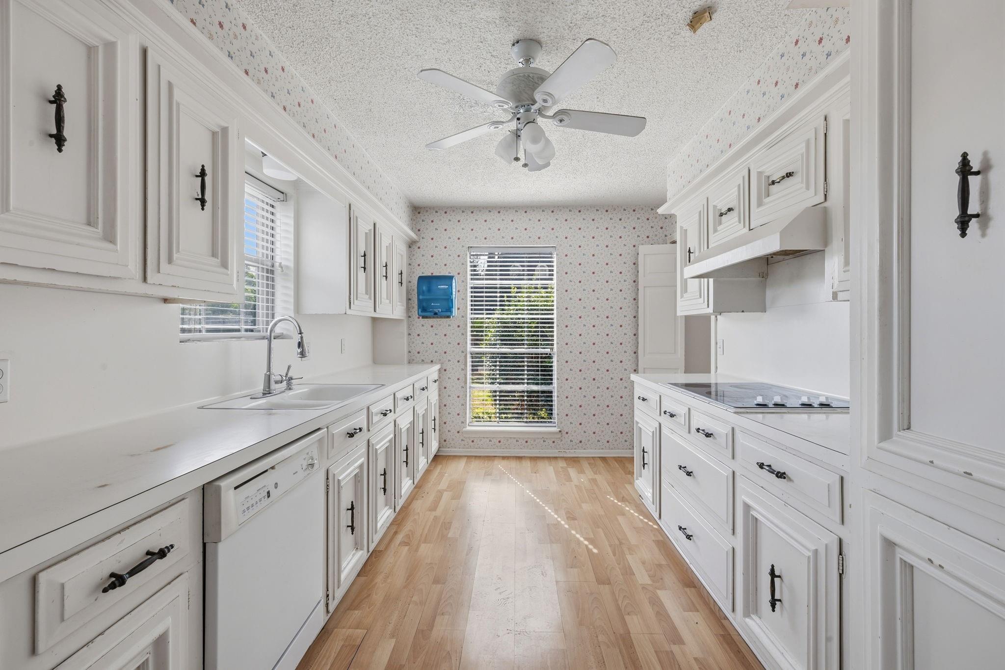 Galley kitchen with white cabinets, floral wallpaper, and light wood floors.