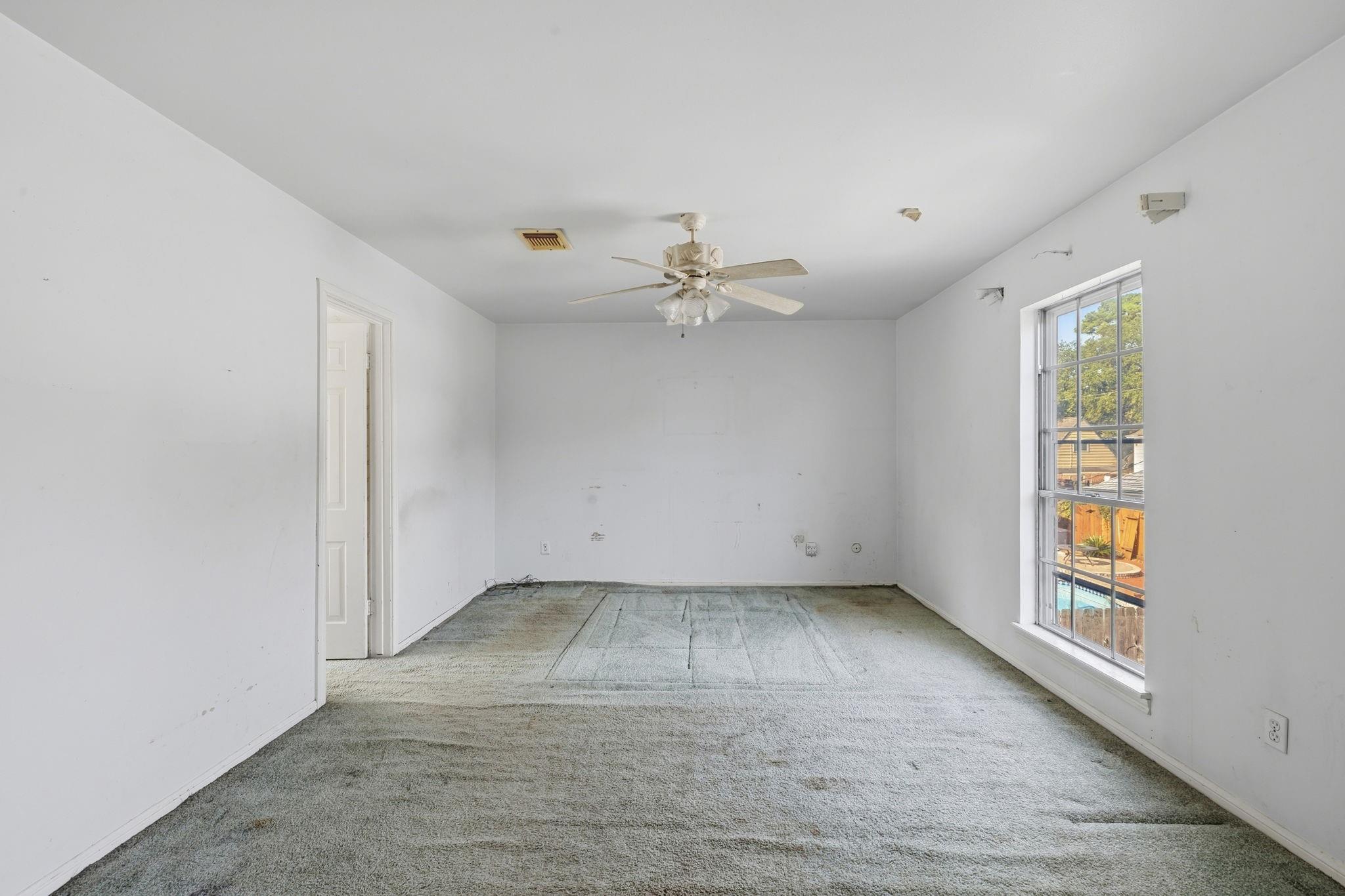 Empty carpeted room with a ceiling fan and a large window overlooking a backyard pool.