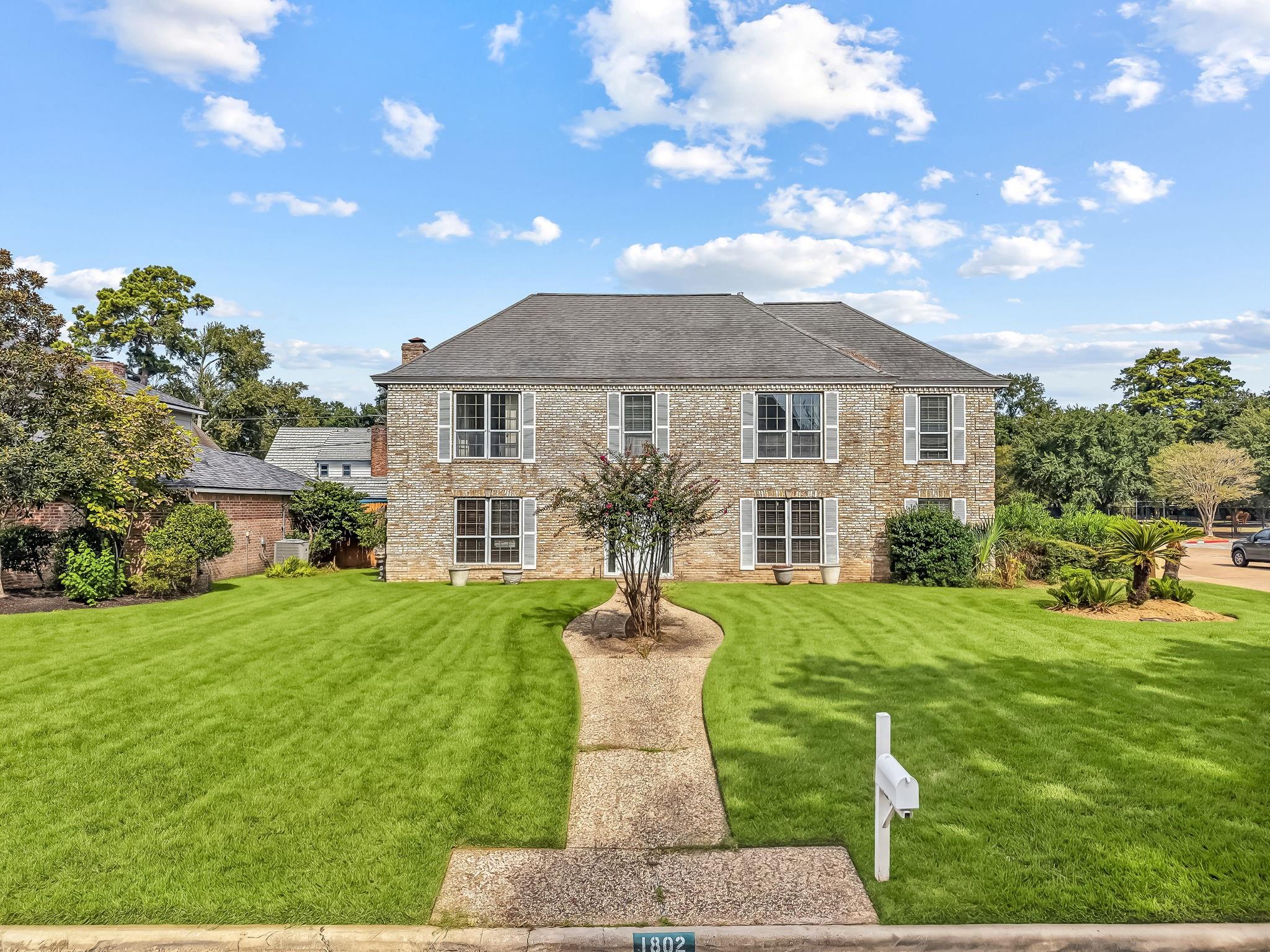 Two-story brick house with white shutters, a curved walkway, and a broad green lawn.