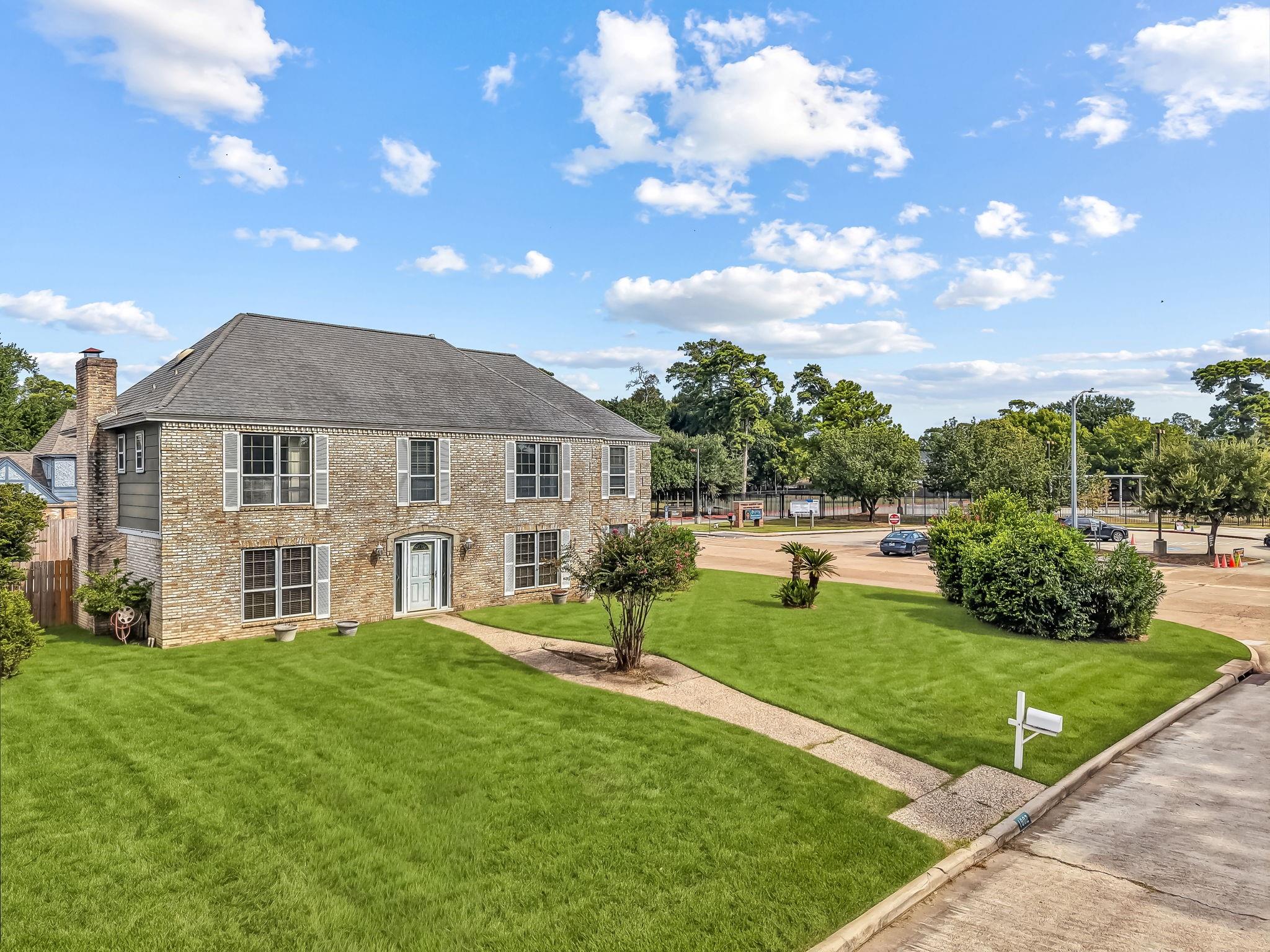 Two-story brick house with a gray roof, chimney, and broad green front lawn.