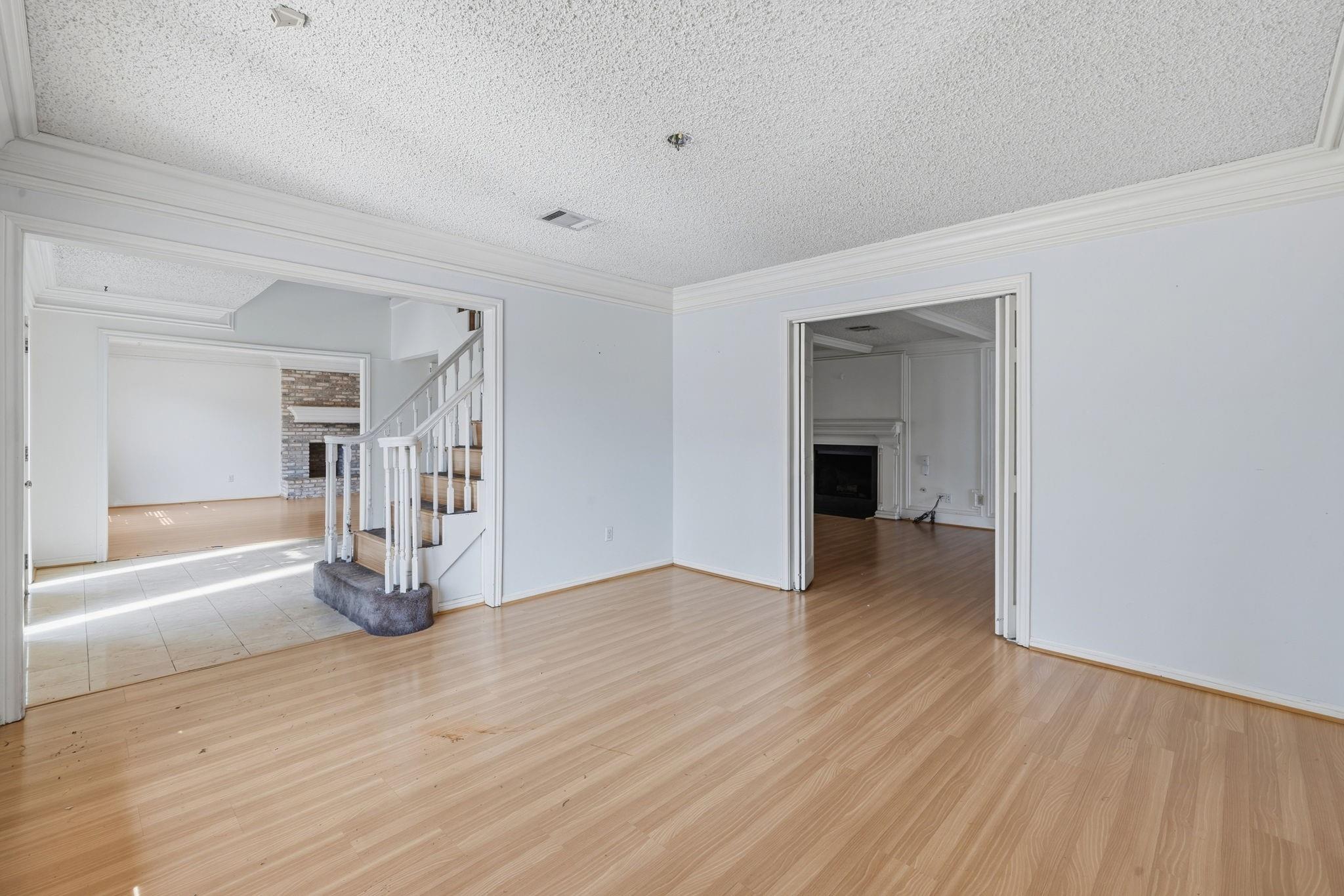 Empty room with light wood floors, opening to a staircase and brick fireplace