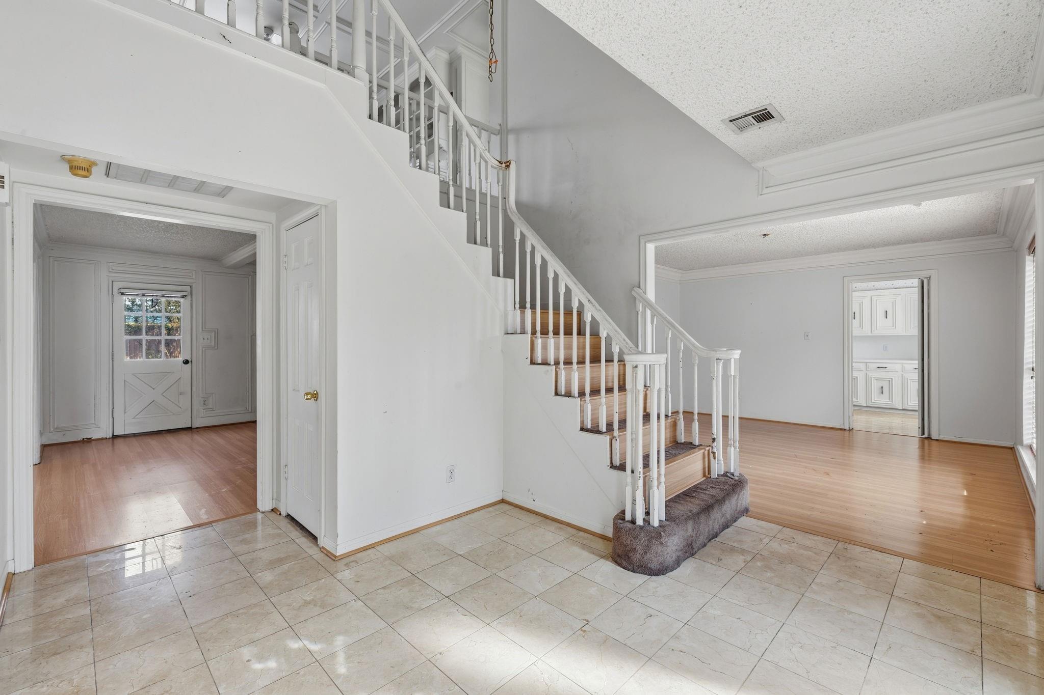 Vacant entryway with tiled floor, white staircase, and adjoining hardwood-floored living area.