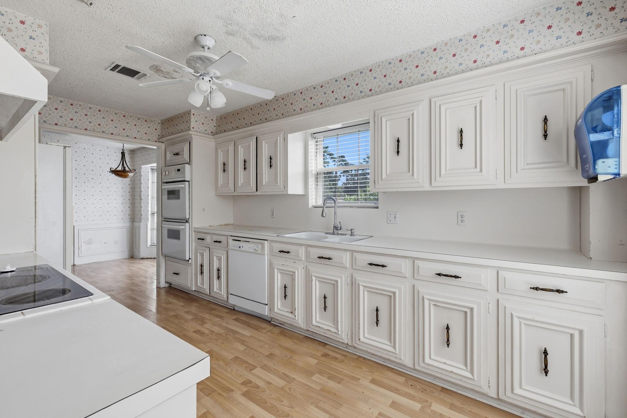 Kitchen with white cabinets, double wall oven, and floral wallpaper bordering the ceiling.