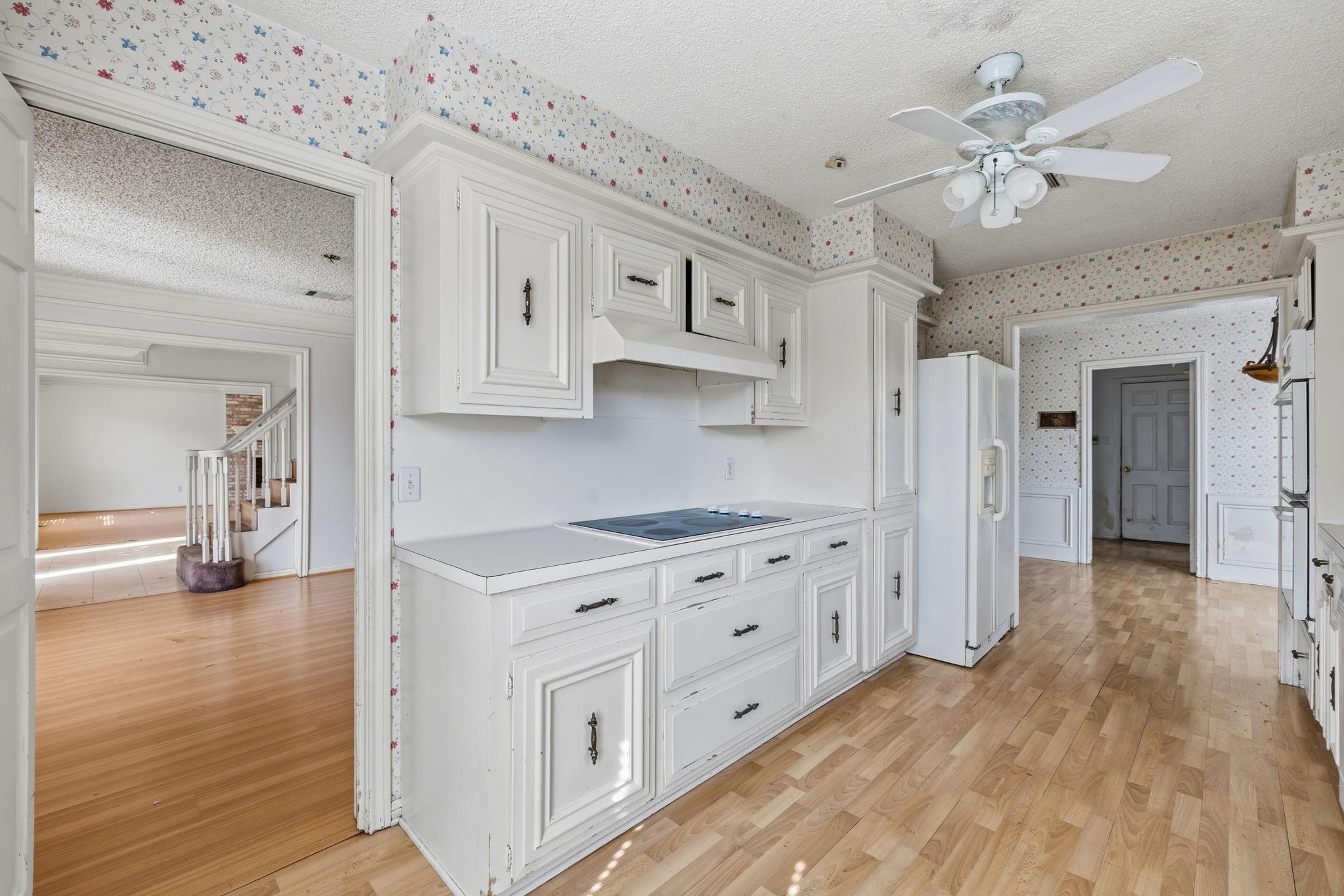 Kitchen with white cabinets, floral wallpaper, a built-in cooktop, and light wood-pattern flooring.