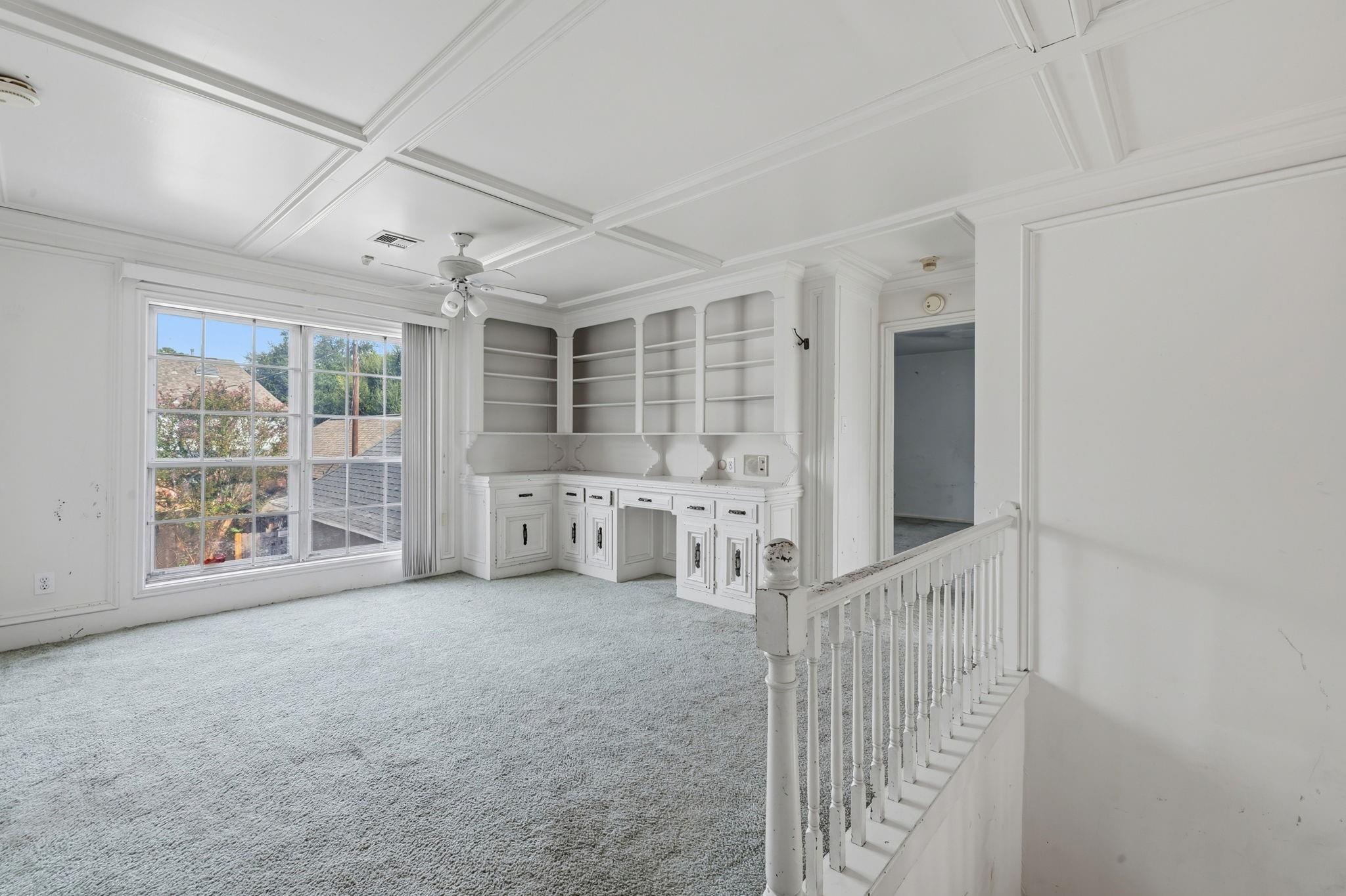 Empty upstairs room with built-in white shelving, a coffered ceiling, and a large window.