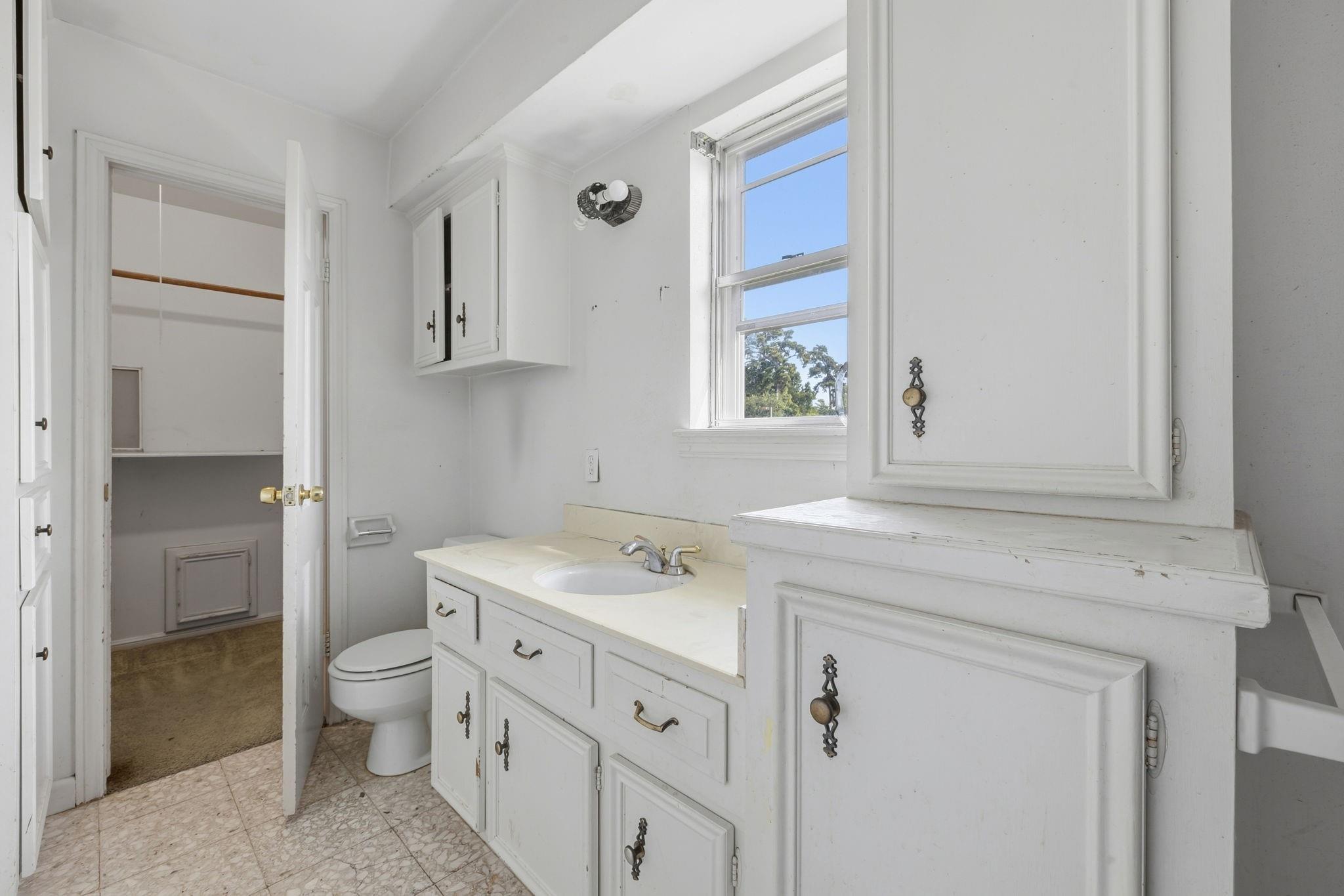 Bathroom with a white built-in vanity, oval sink, toilet, and a sunlit window.