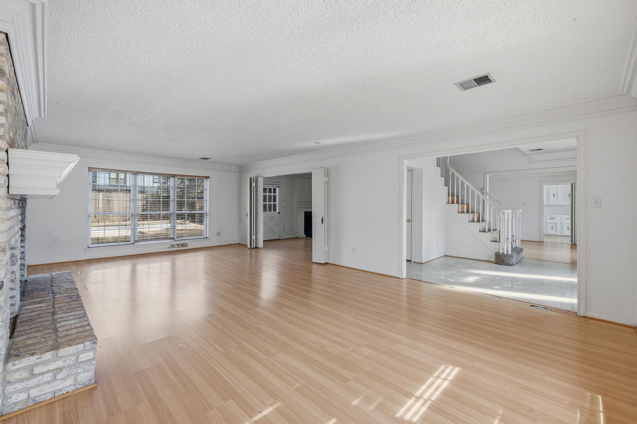 Unfurnished living room with light wood floors, a white brick fireplace, and a view toward the staircase.
