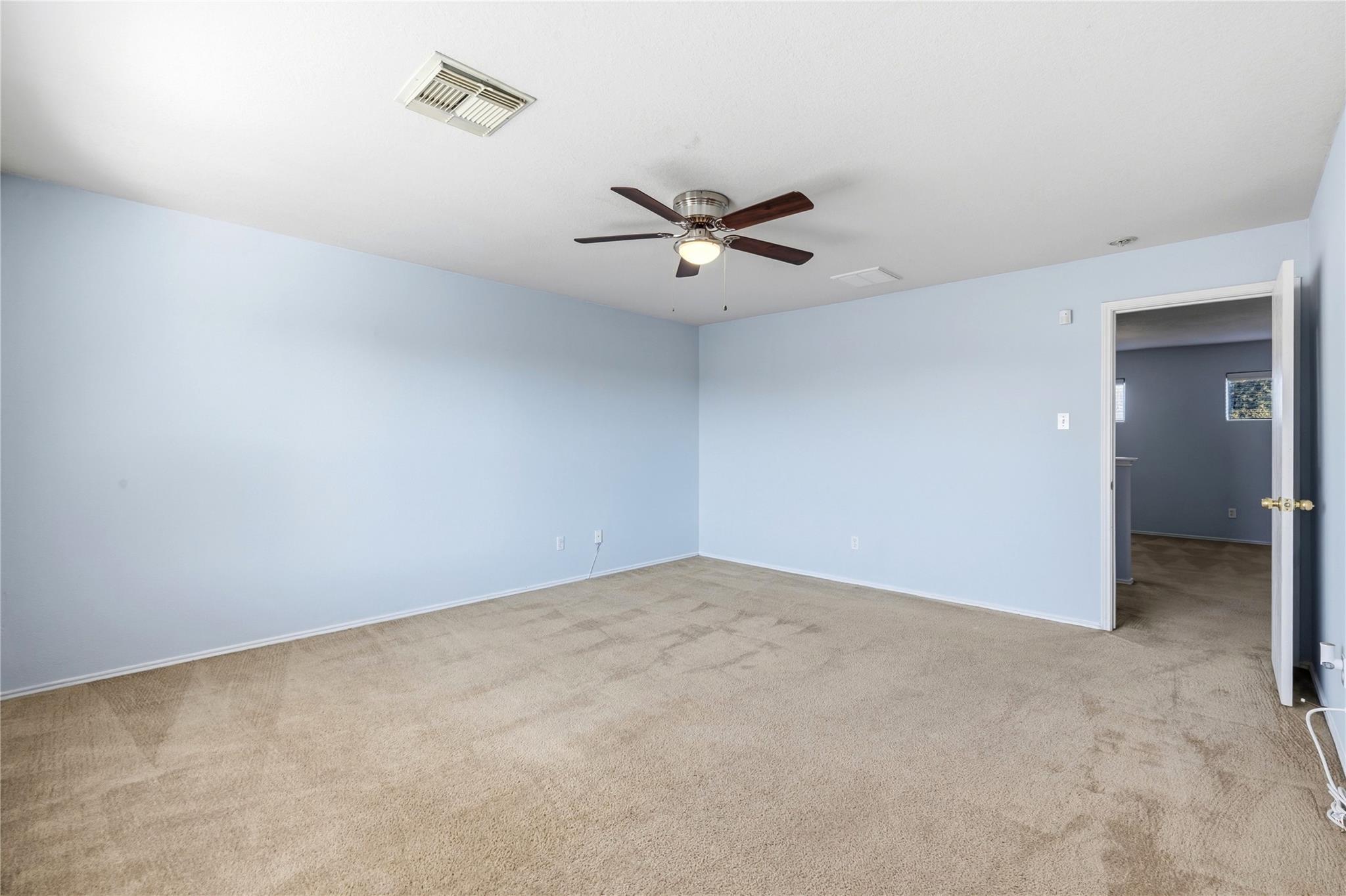 Empty blue bedroom with beige carpet, a ceiling fan, and an open doorway.