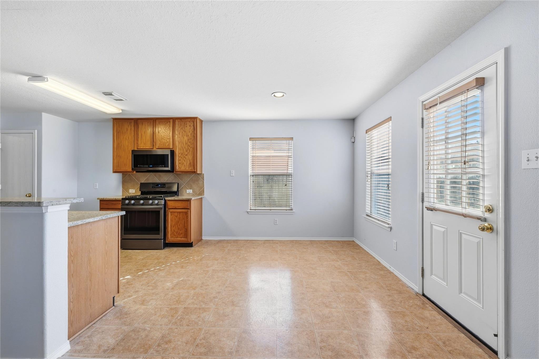 Empty kitchen with wood cabinets, stainless appliances, a breakfast bar, and tan tile flooring.