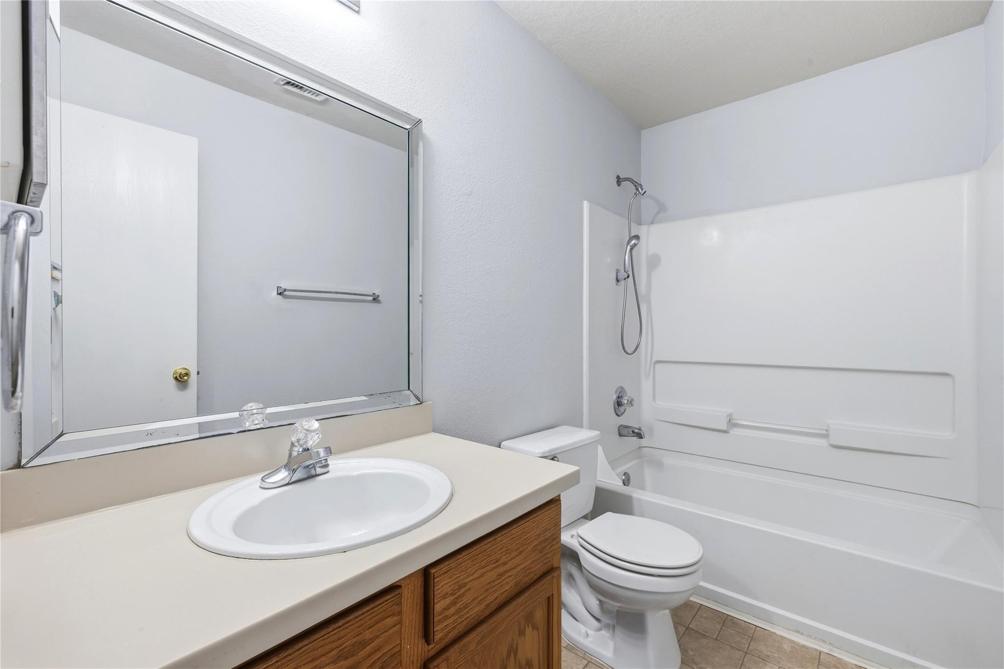 Bathroom with a wood vanity, large mirror, and white tub-shower beside the toilet.