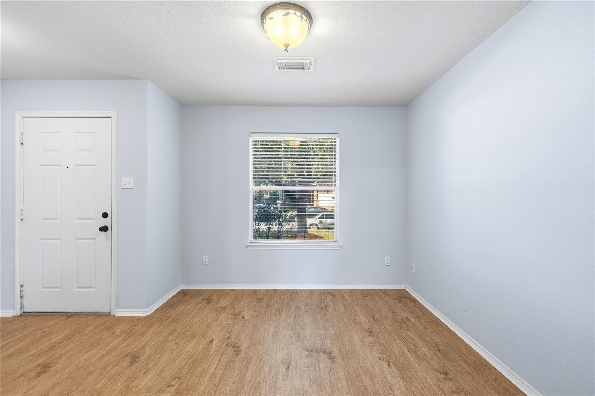 Empty room with pale blue walls, wood-look flooring, and a window with blinds.
