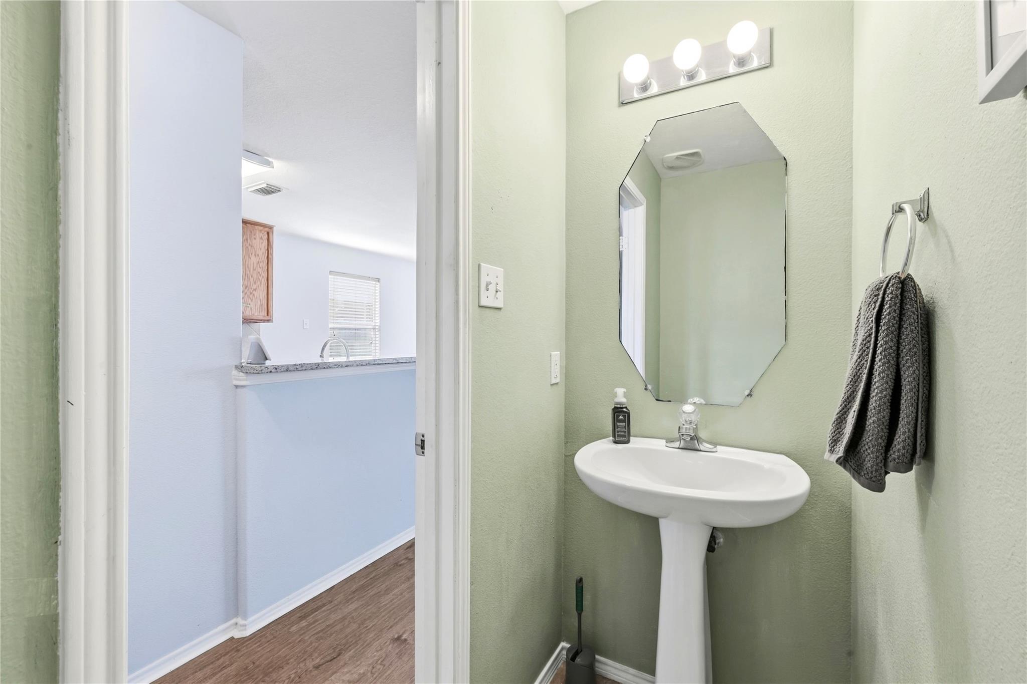 Bathroom with a pedestal sink and angular mirror, opening onto a kitchen with a pass-through counter.