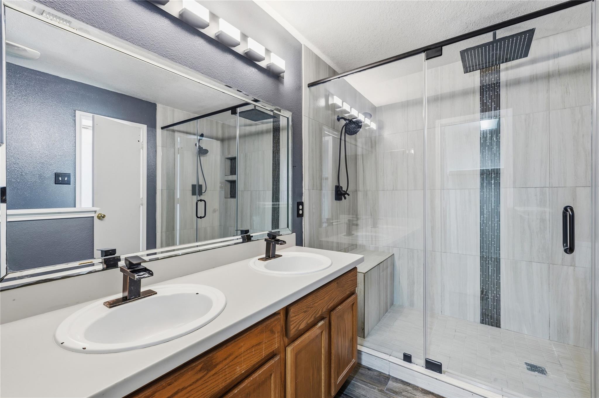 Bathroom with a double-sink wood vanity and glass walk-in shower with black fixtures.