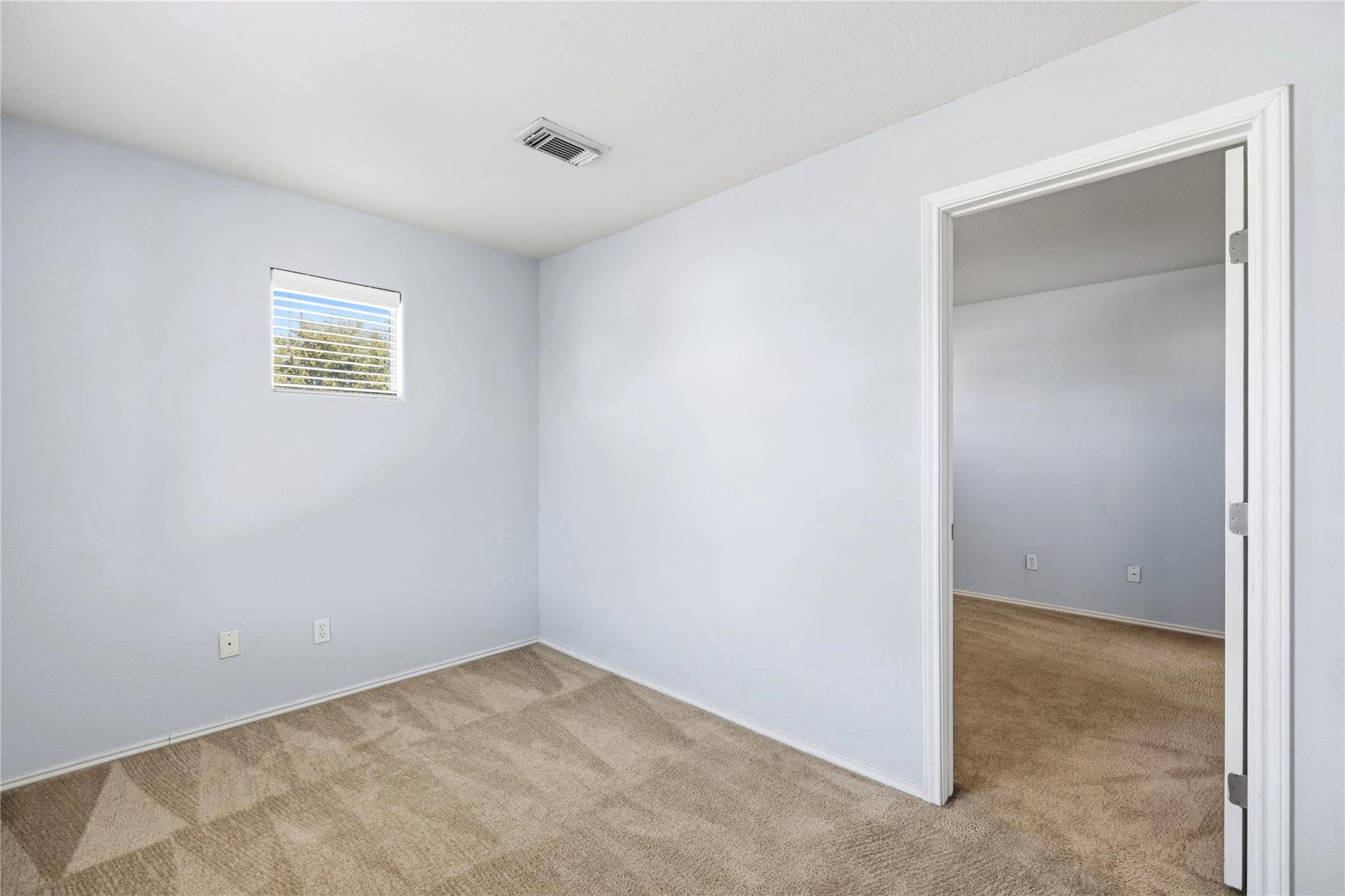 Vacant carpeted room with a small window and an open doorway to an adjoining room.