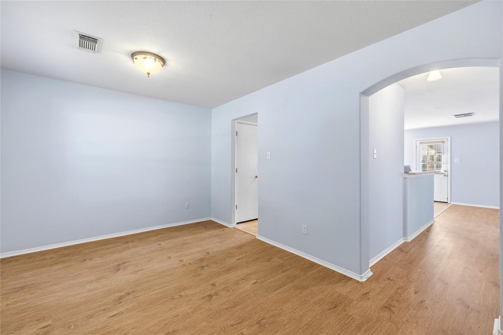 Empty room with wood-look flooring and an arched opening to the kitchen.