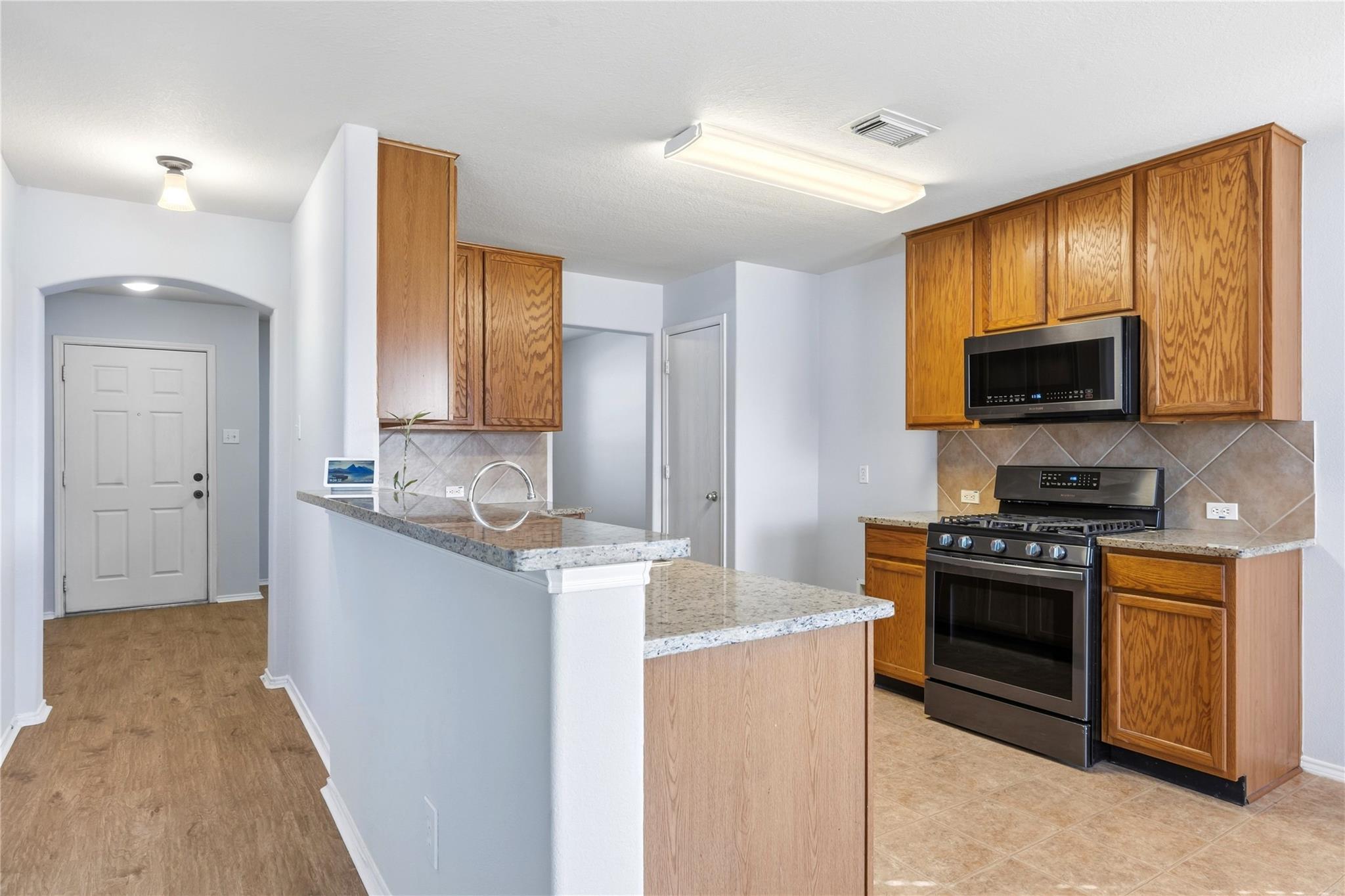 Kitchen with oak cabinets, granite breakfast bar, stainless steel range, and tiled backsplash.