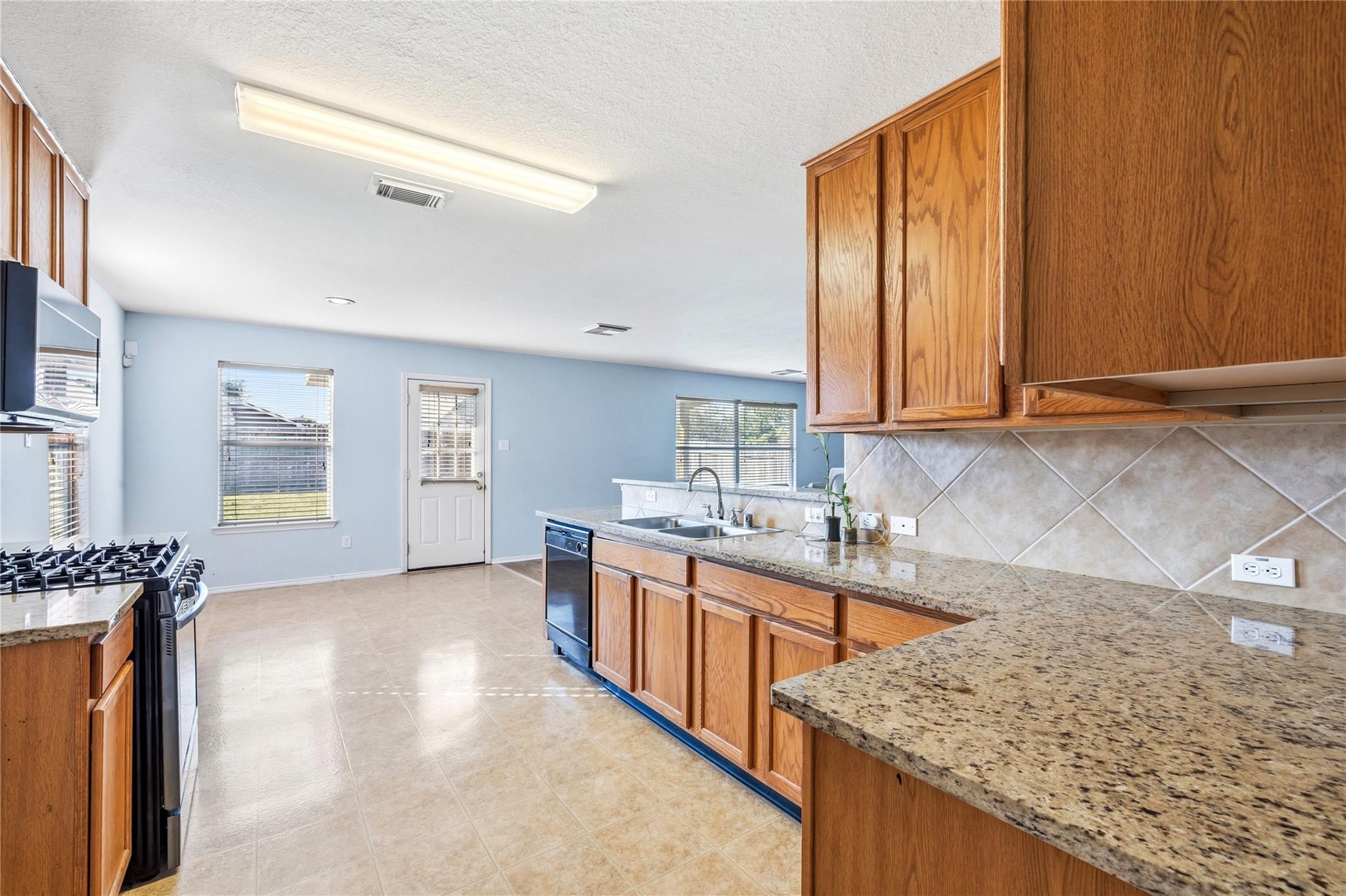 Kitchen with honey-toned wood cabinets, granite counters, diagonal tile backsplash, and a gas range.
