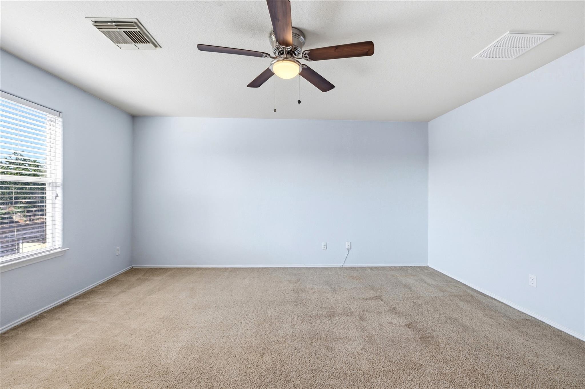 Empty carpeted bedroom with pale blue walls, window blinds, and a dark wood ceiling fan.
