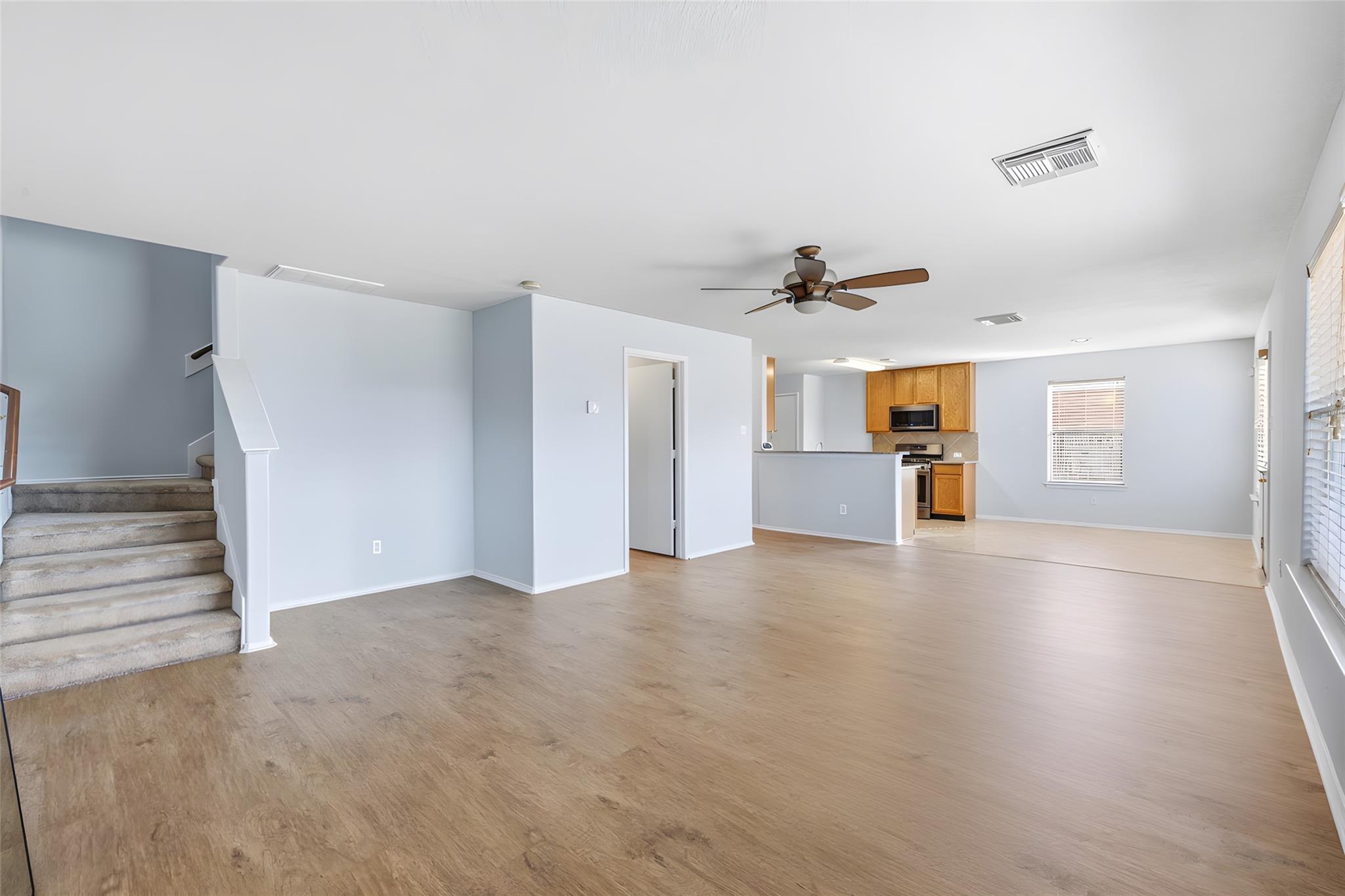 Open living area with wood-look floors, carpeted stairs, and a kitchen with wood cabinets.
