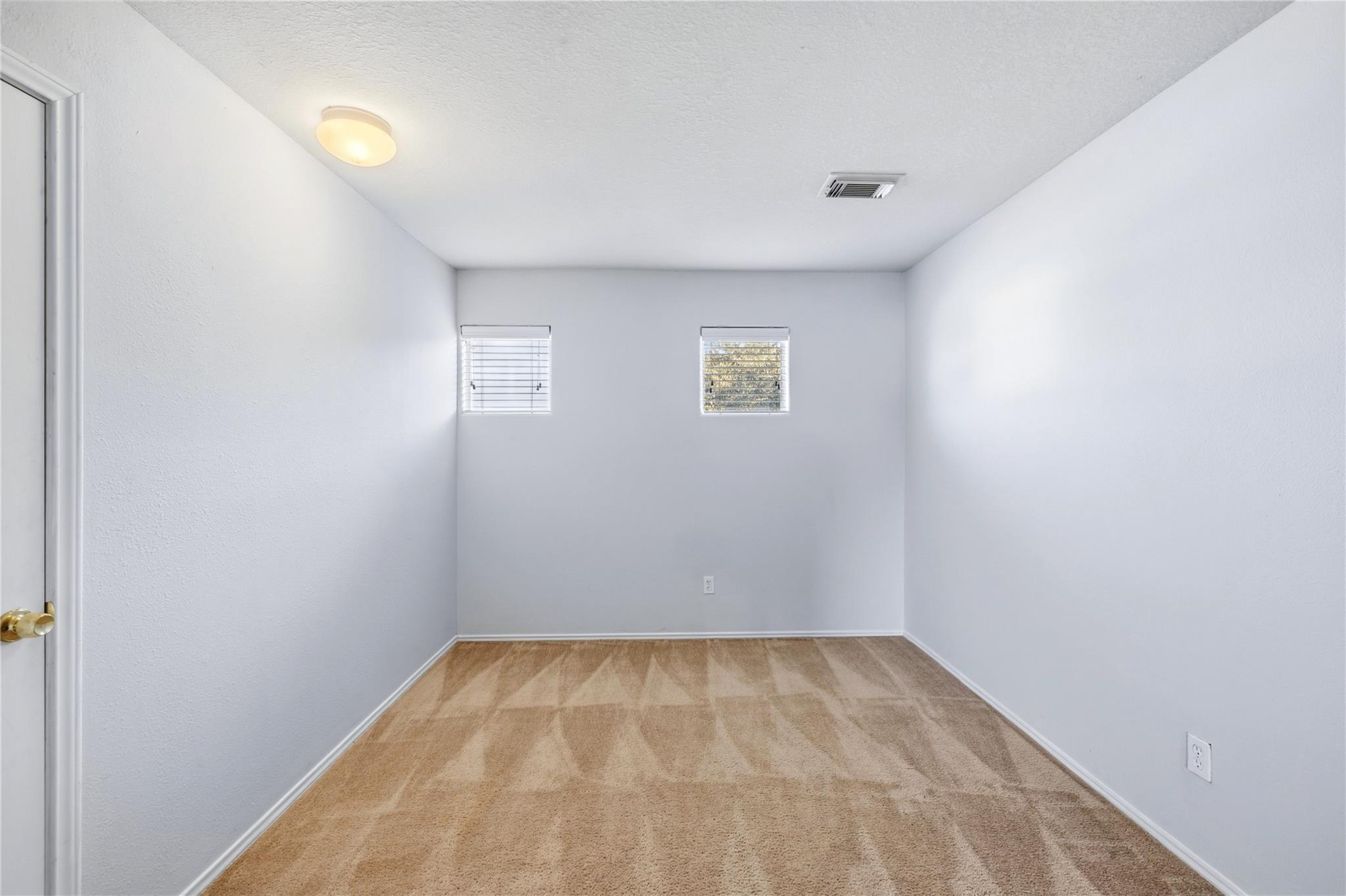 Empty carpeted room with two windows and a ceiling light.