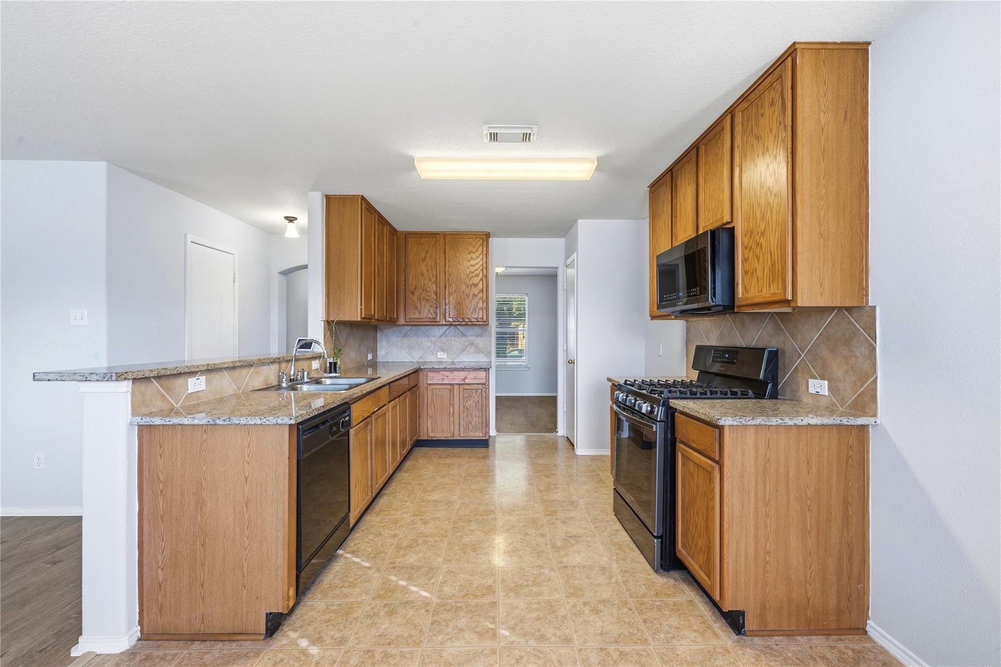 Vacant kitchen with oak cabinets, granite counters, tan tile, and black appliances.