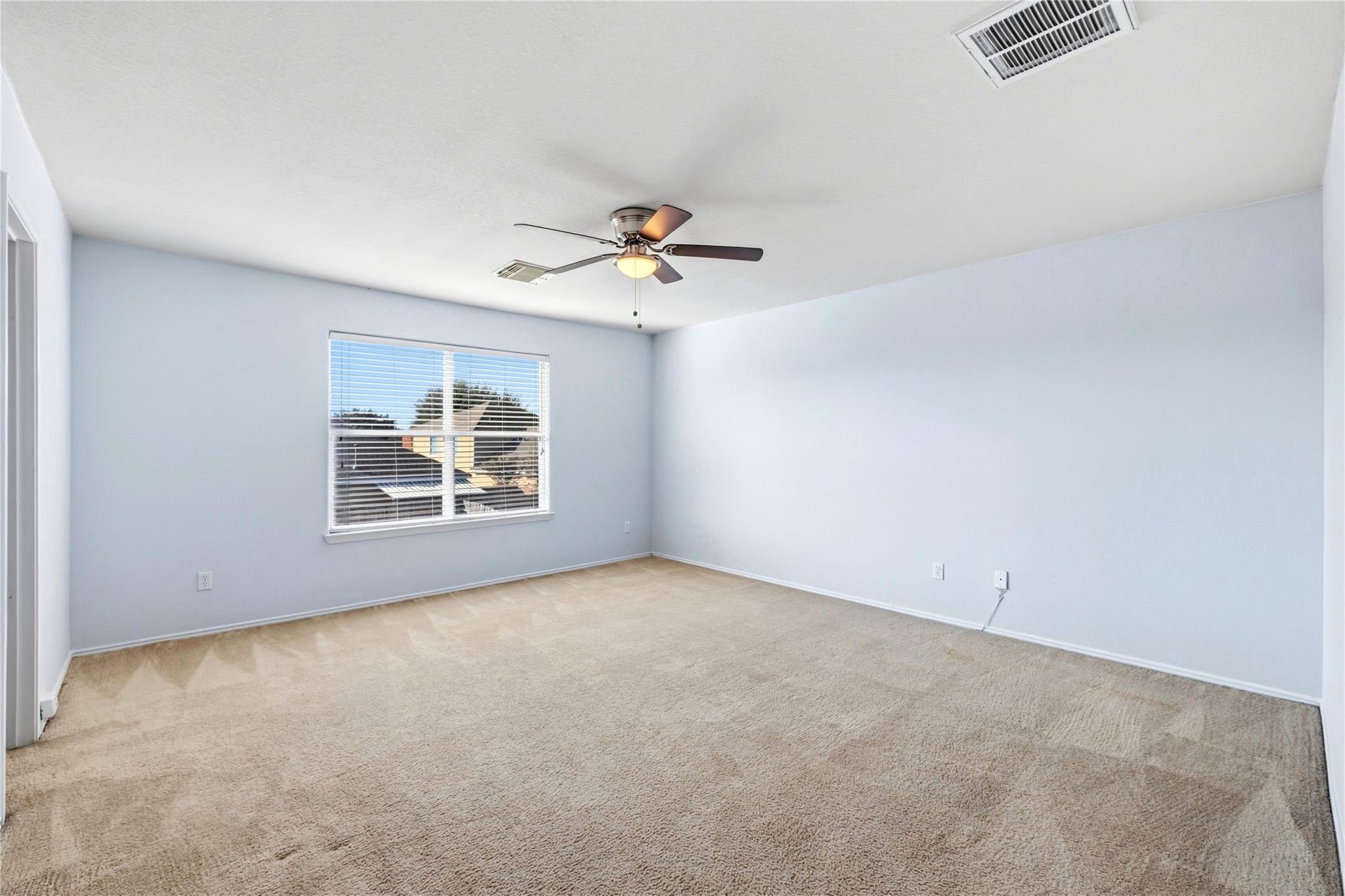 Empty bedroom with pale blue walls, beige carpet, window blinds, and a ceiling fan.