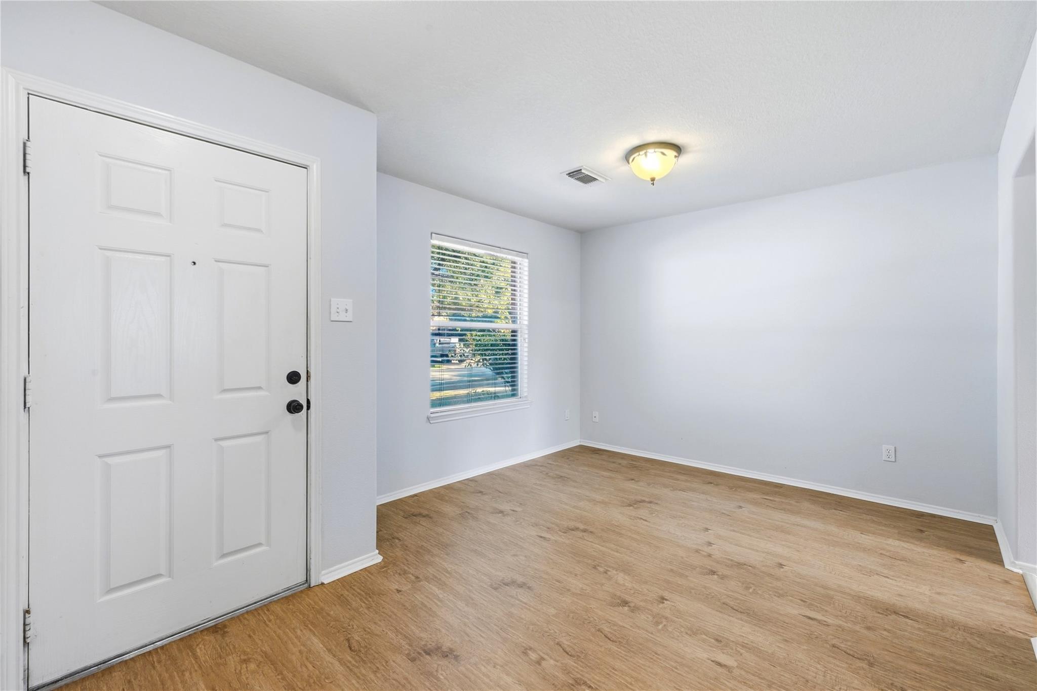 Empty entry room with a white paneled front door, window with blinds, and wood-look flooring.