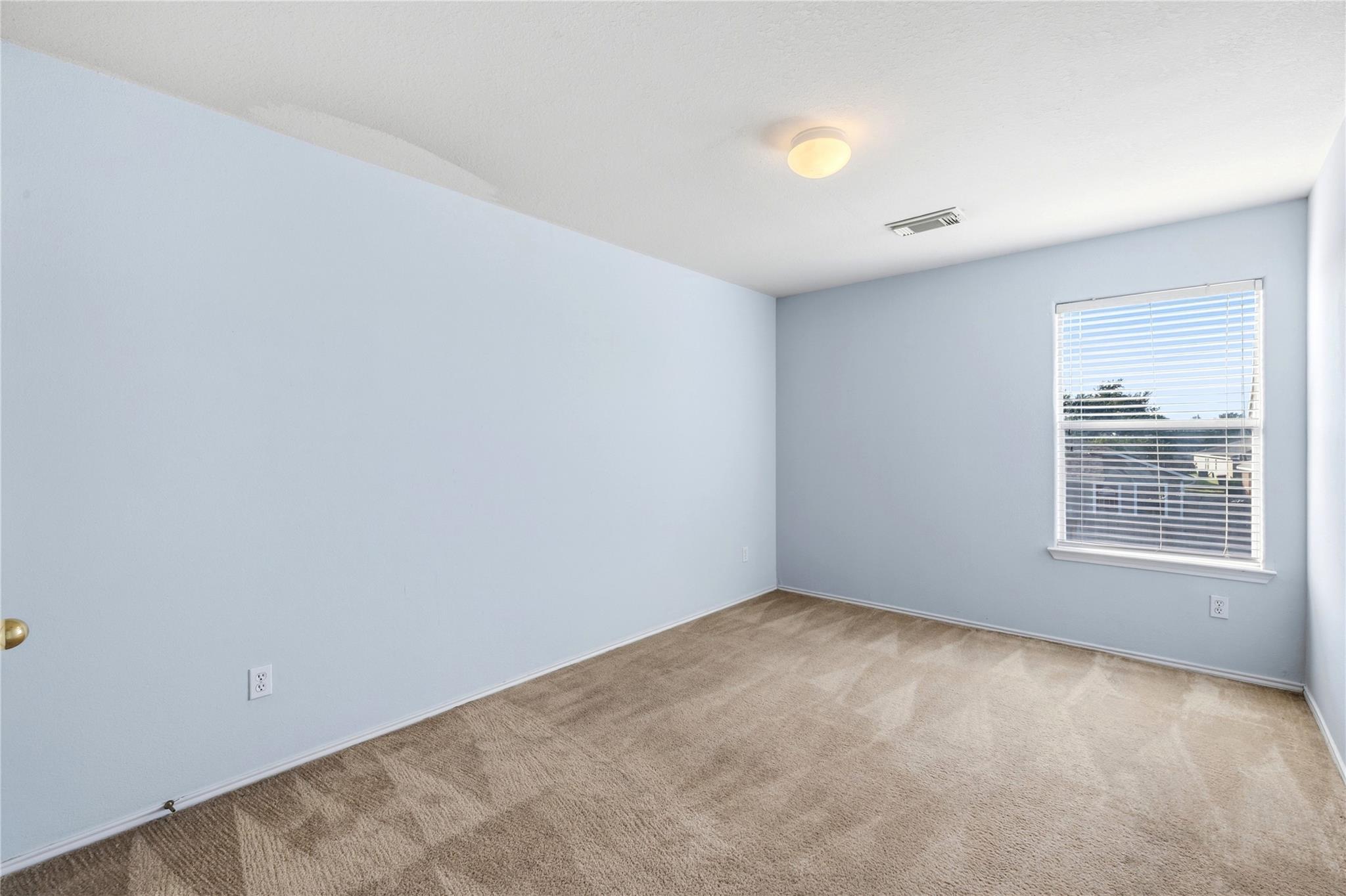 Empty bedroom with pale blue walls, beige carpet, and a window with white blinds.