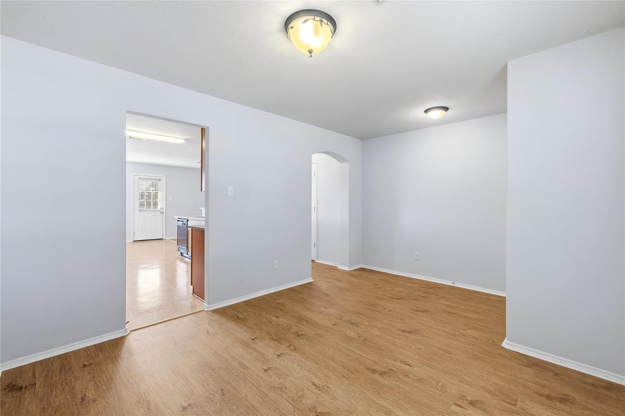 Vacant room with wood-look flooring, opening to a tiled kitchen.